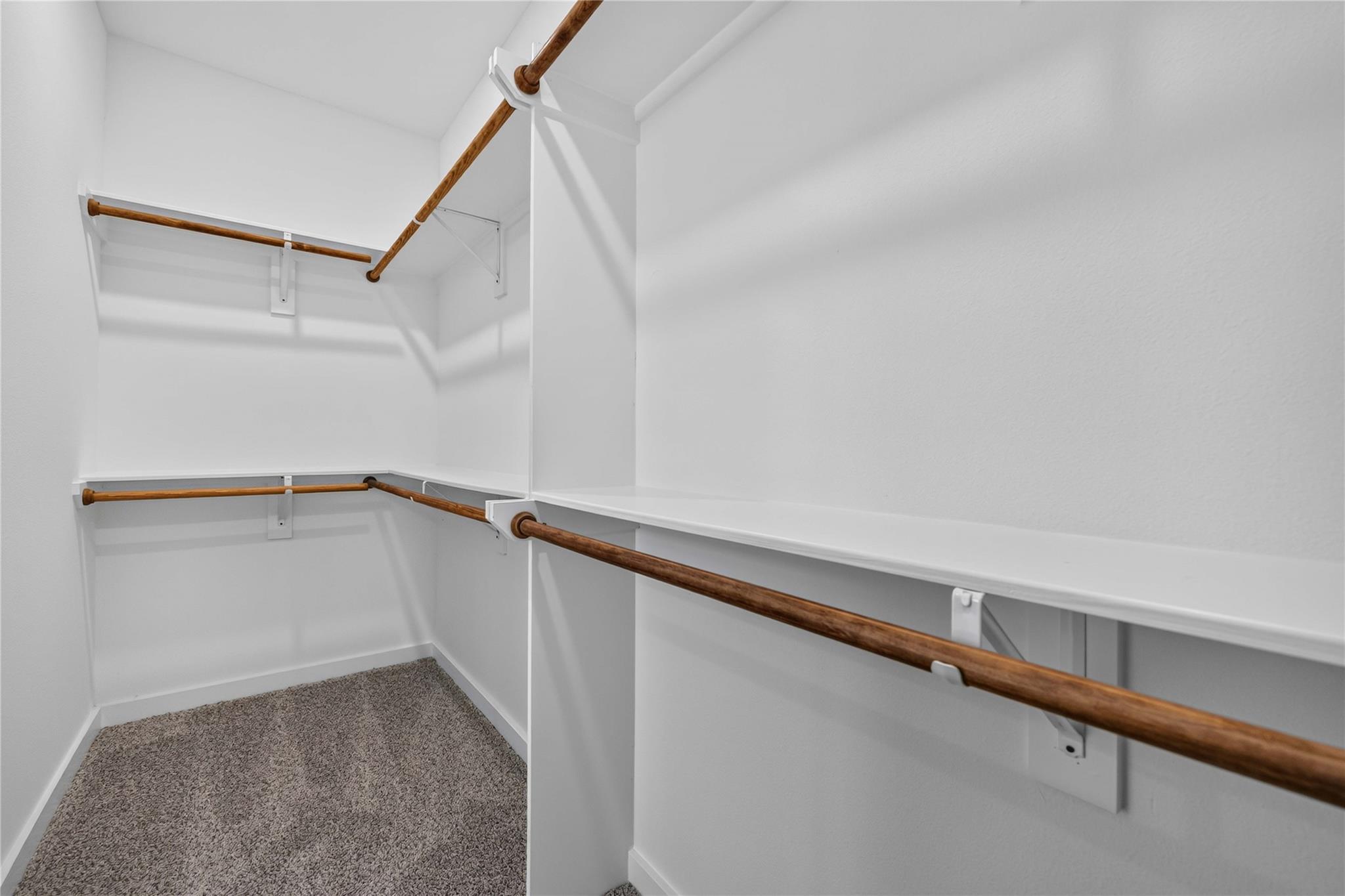 Walk-in closet with built-in shelves, multiple wooden hanging rods, and gray carpet.