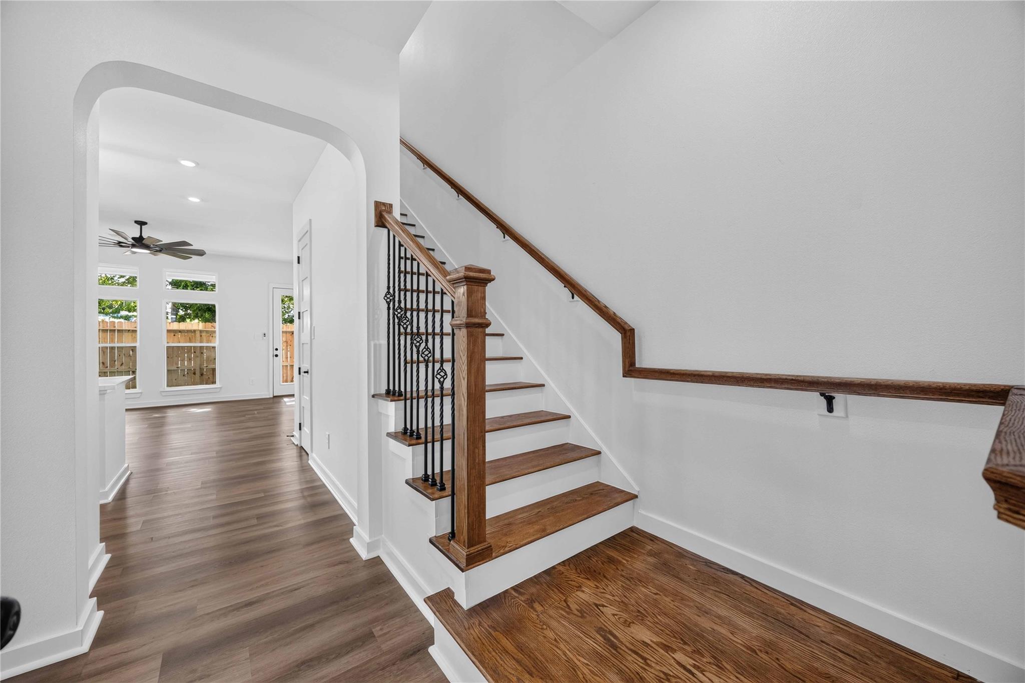 Staircase with wood treads and black metal balusters beside a bright room with large windows.
