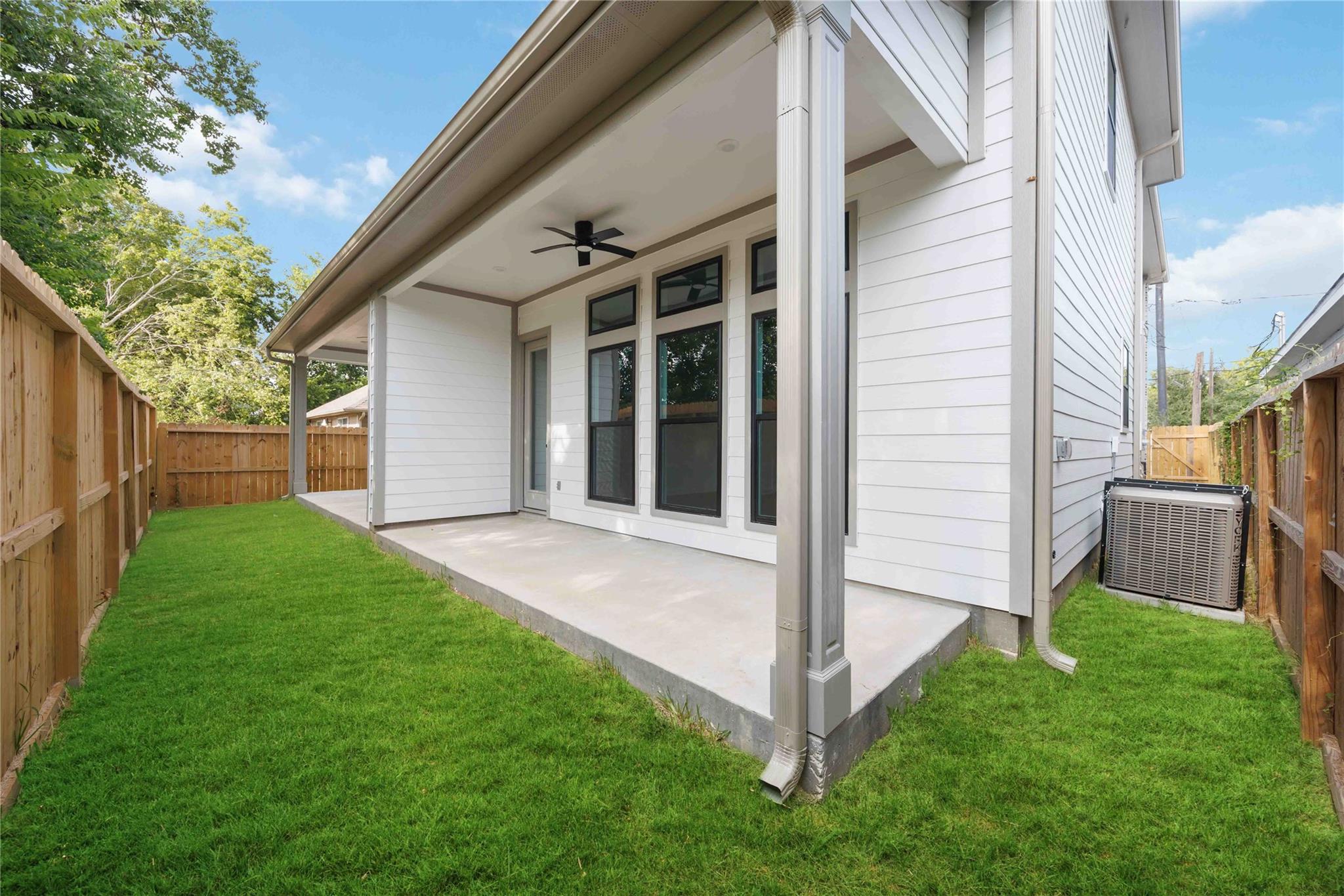 Covered concrete patio and white-sided house overlooking a fenced, grassy backyard.