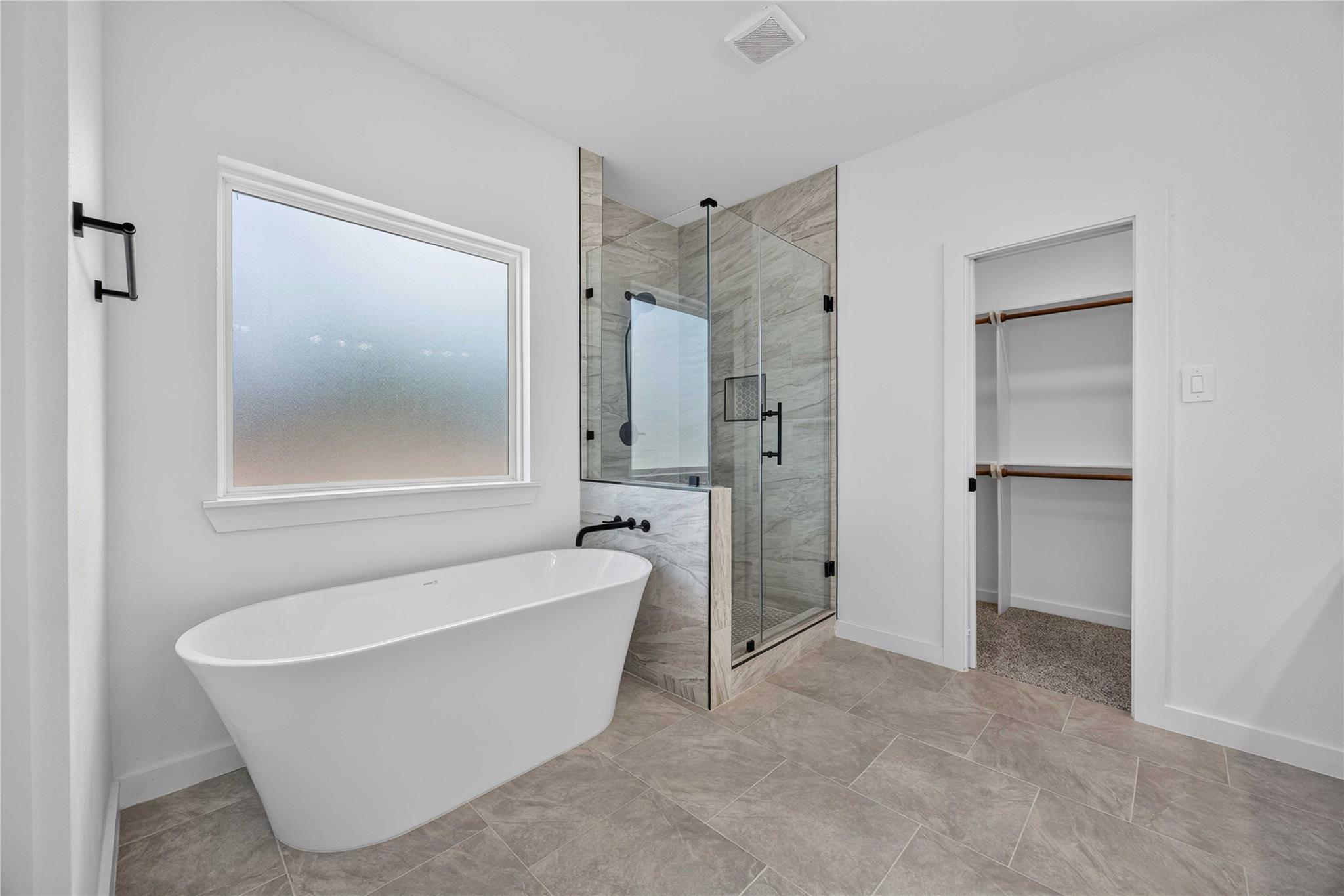 Bathroom with a freestanding soaking tub, glass shower, and gray stone tile.