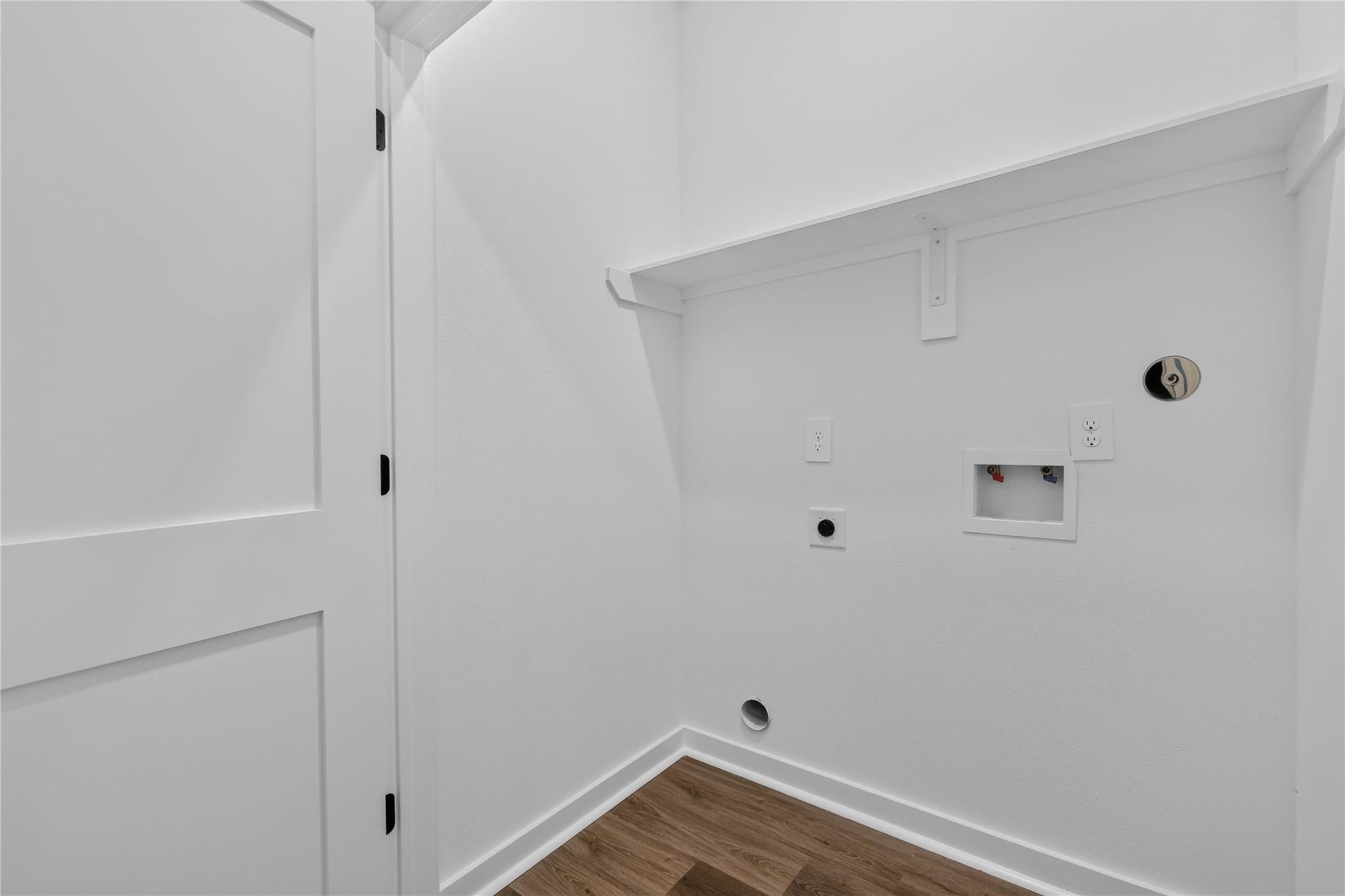 Empty laundry area with washer and dryer hookups beneath a wall shelf.