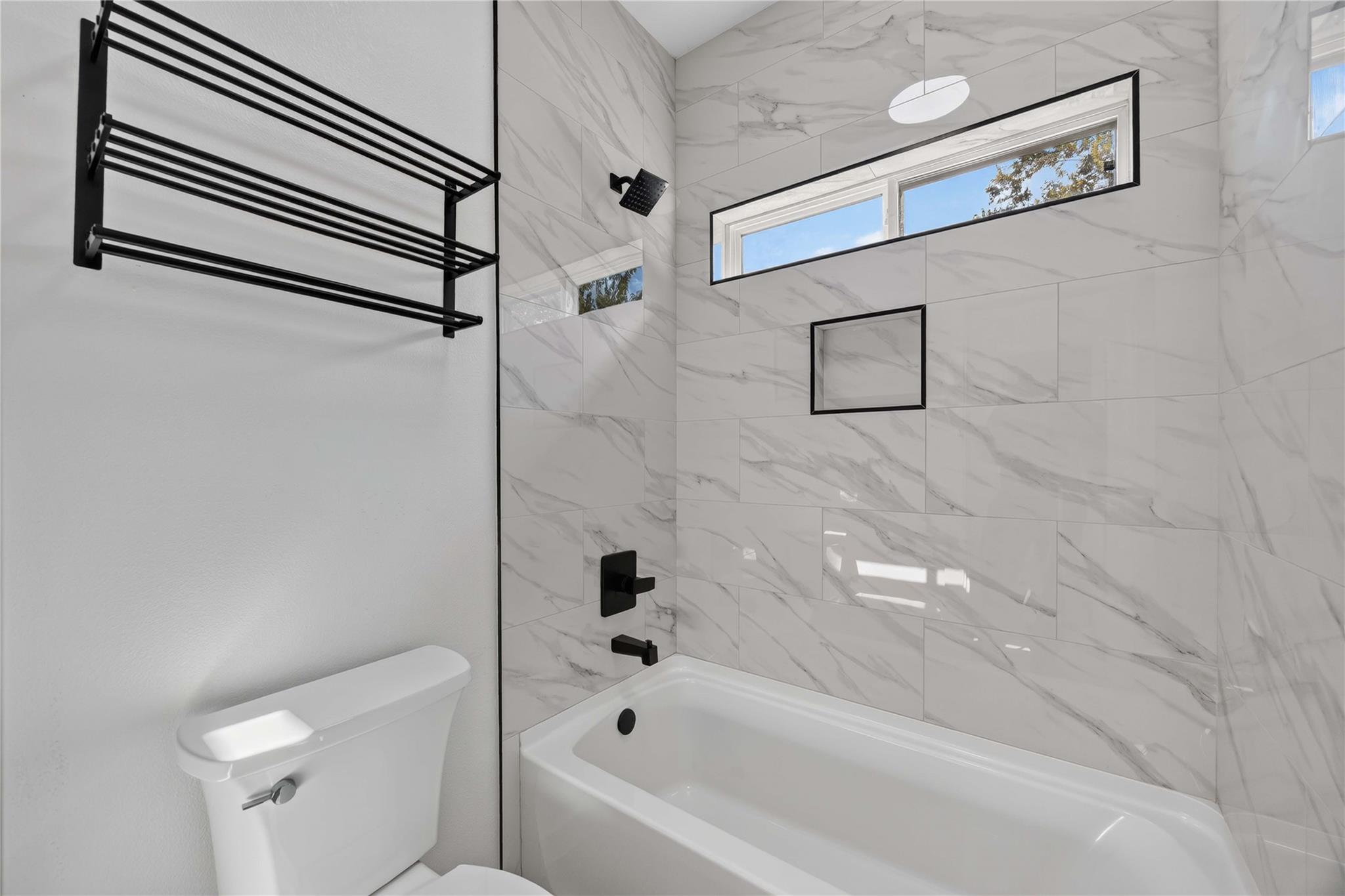 Bathroom with marble-look tile, a white tub, matte black fixtures, and a high horizontal window.
