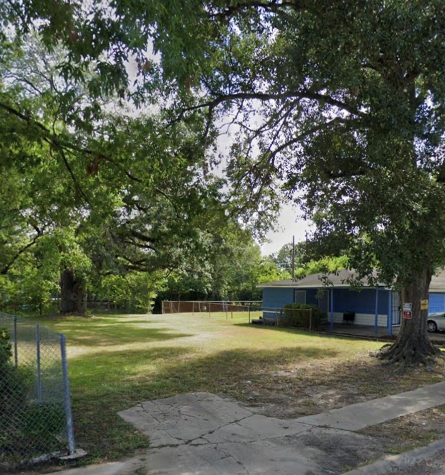 Grassy lot shaded by large trees, with chain-link fencing and a small blue building at the right.