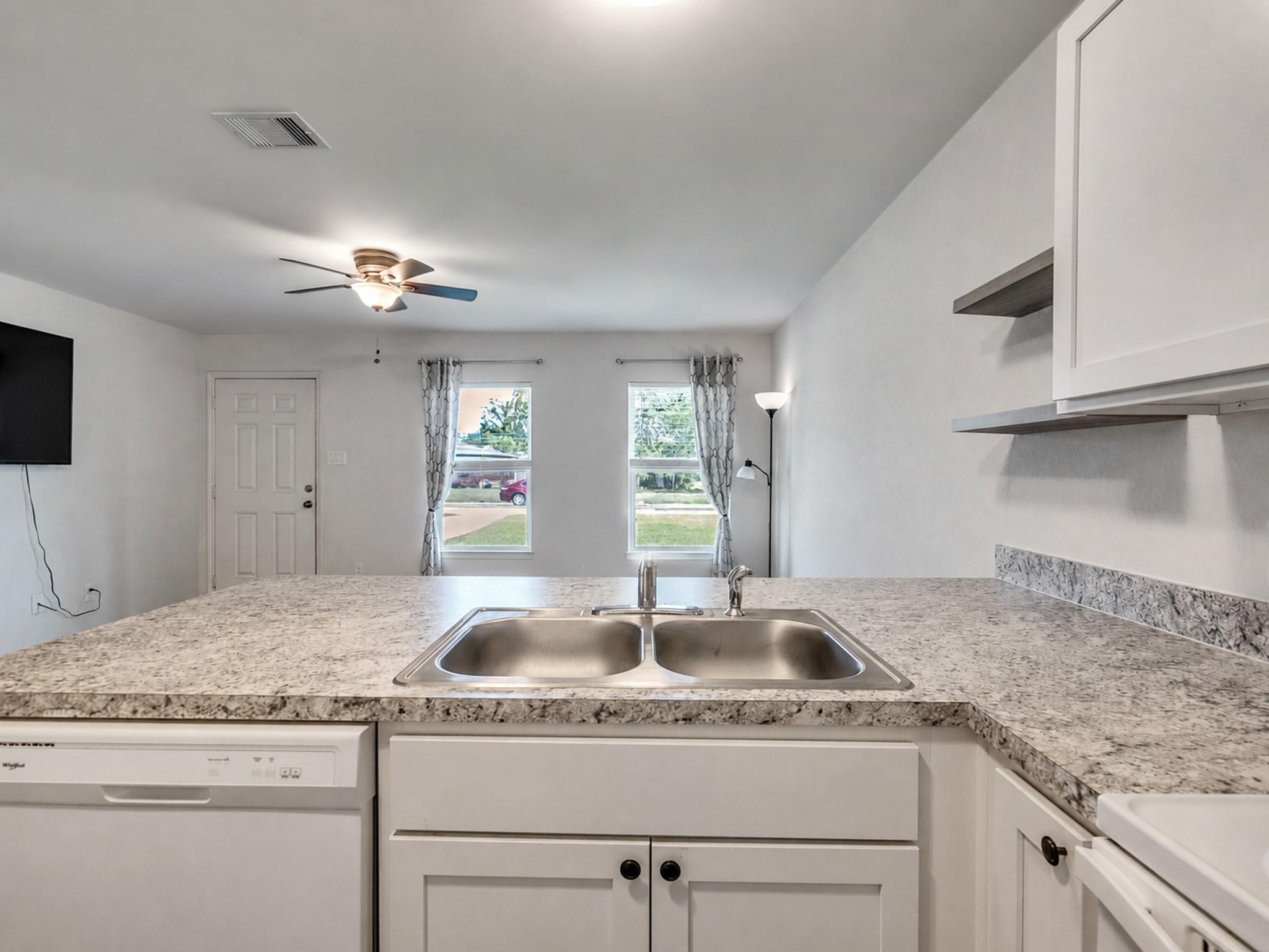 Kitchen with double-basin sink, speckled stone countertop, white cabinets, and dishwasher.