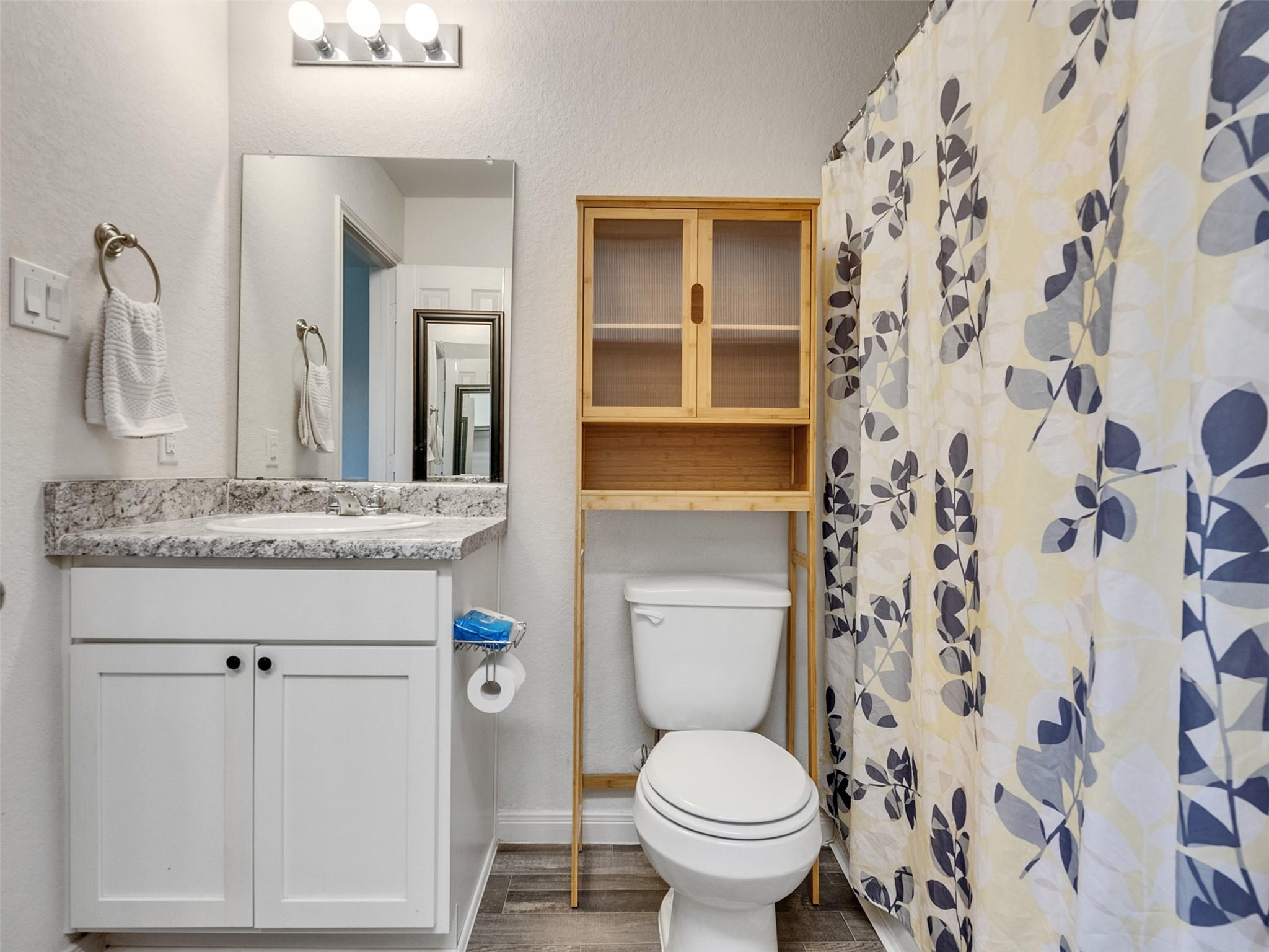 Bathroom with a white vanity, wood storage cabinet above the toilet, and blue-and-white patterned shower curtain.