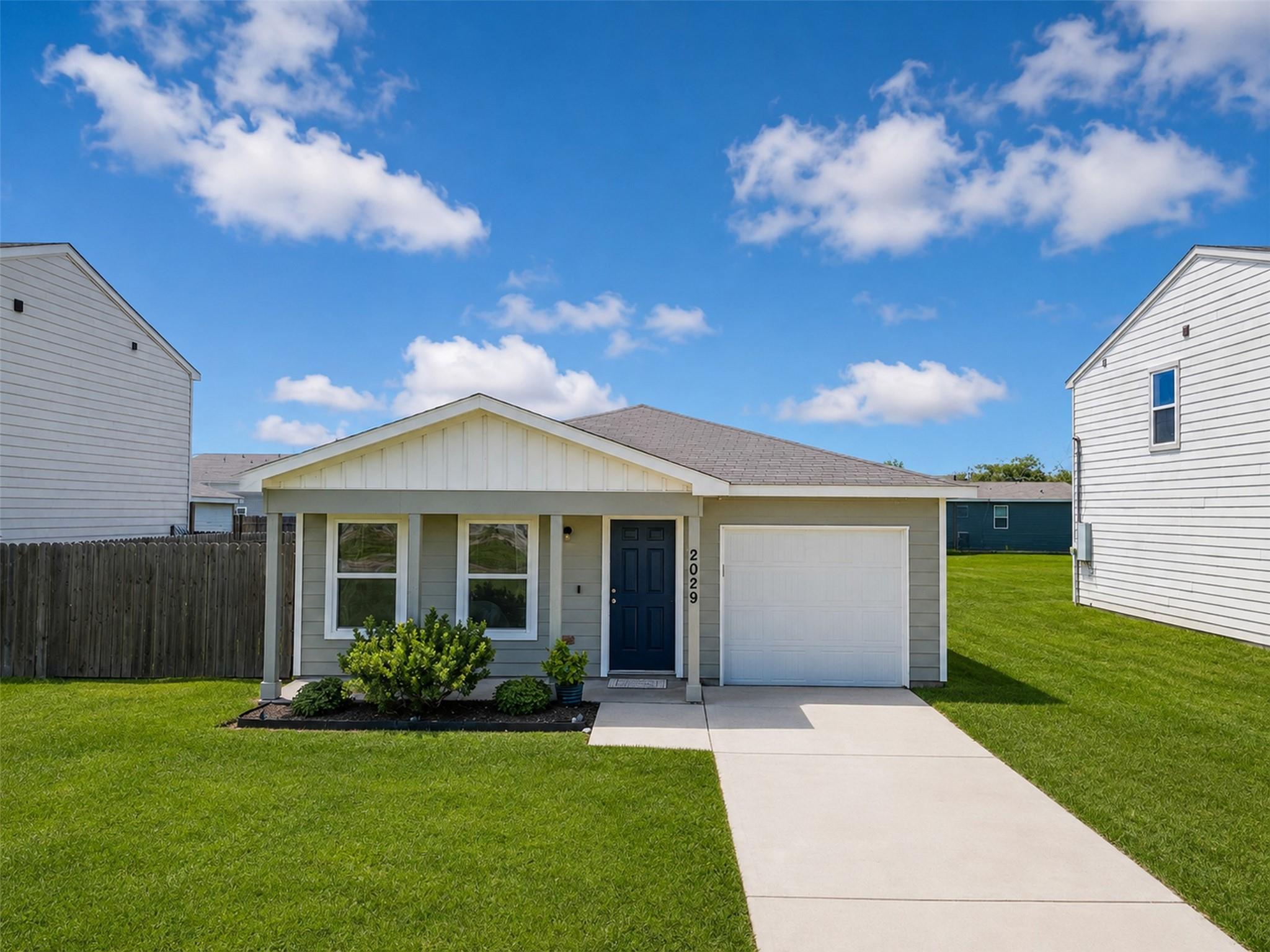 Single-story gray house with a blue front door, attached garage, and broad concrete driveway.