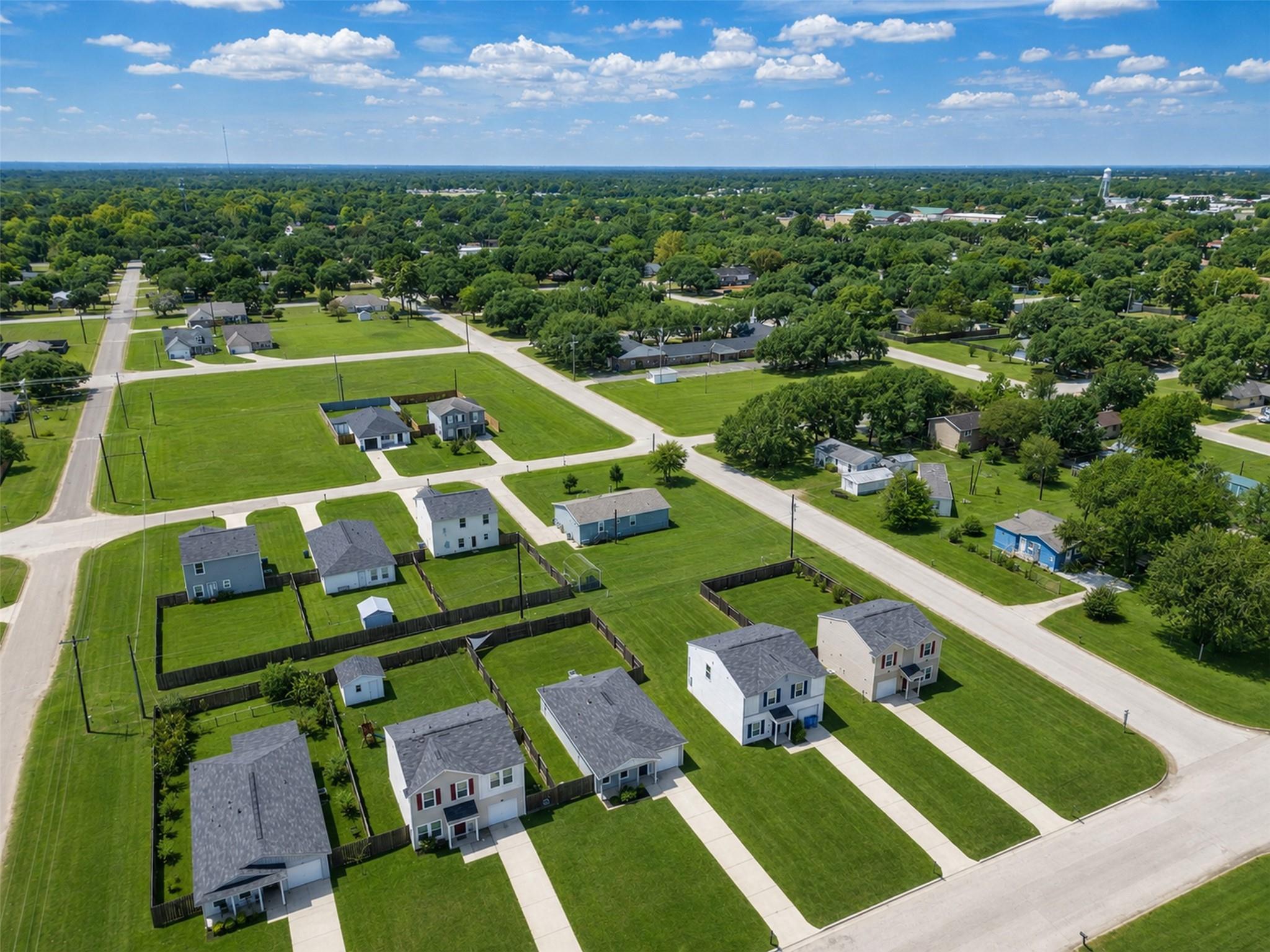 Aerial view of a residential neighborhood with green lawns, detached homes, and a distant water tower.