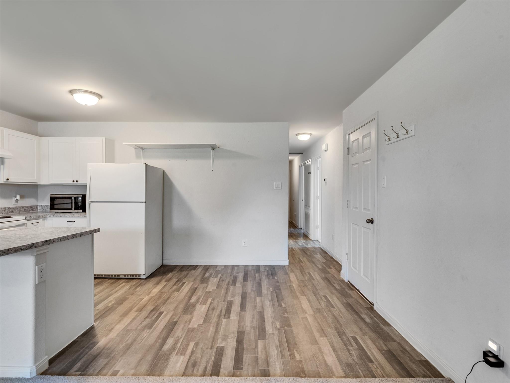 Unfurnished kitchen and dining area with white cabinets, refrigerator, breakfast bar, and wood-look plank flooring.