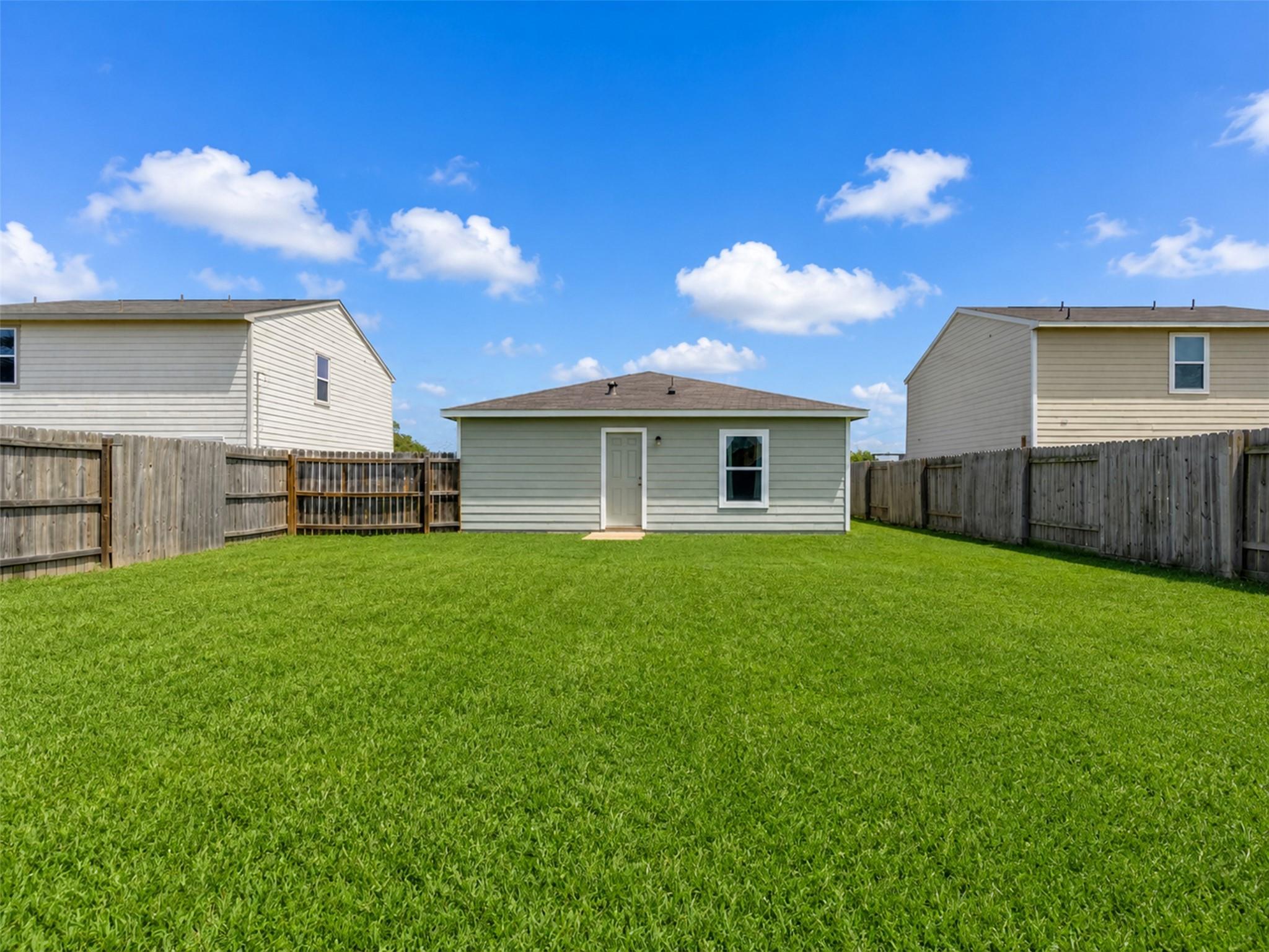 Fenced backyard with a wide green lawn and a small gray outbuilding at the far end.