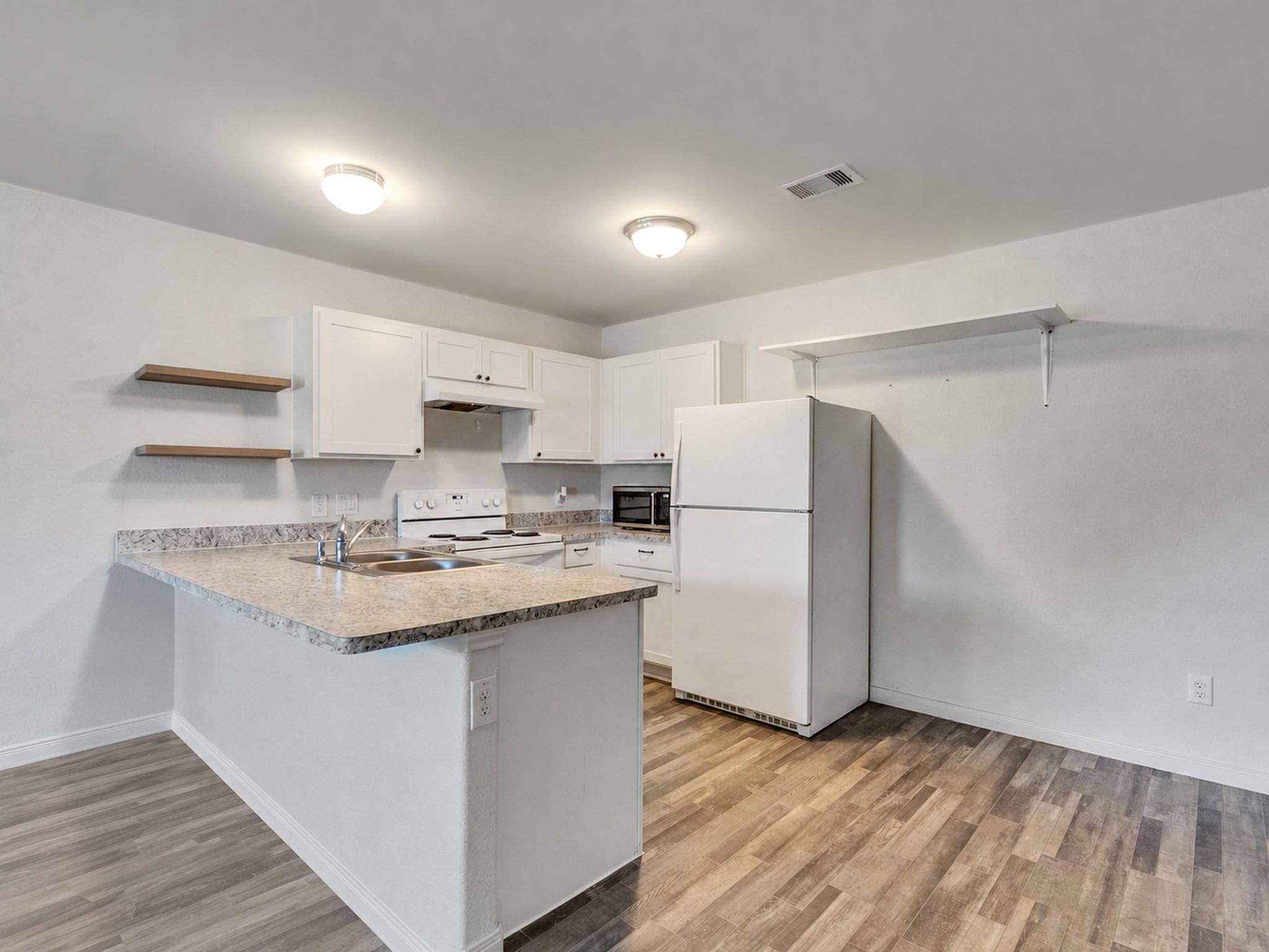 Kitchen with white cabinets, a peninsula sink, refrigerator, and wood-look flooring.