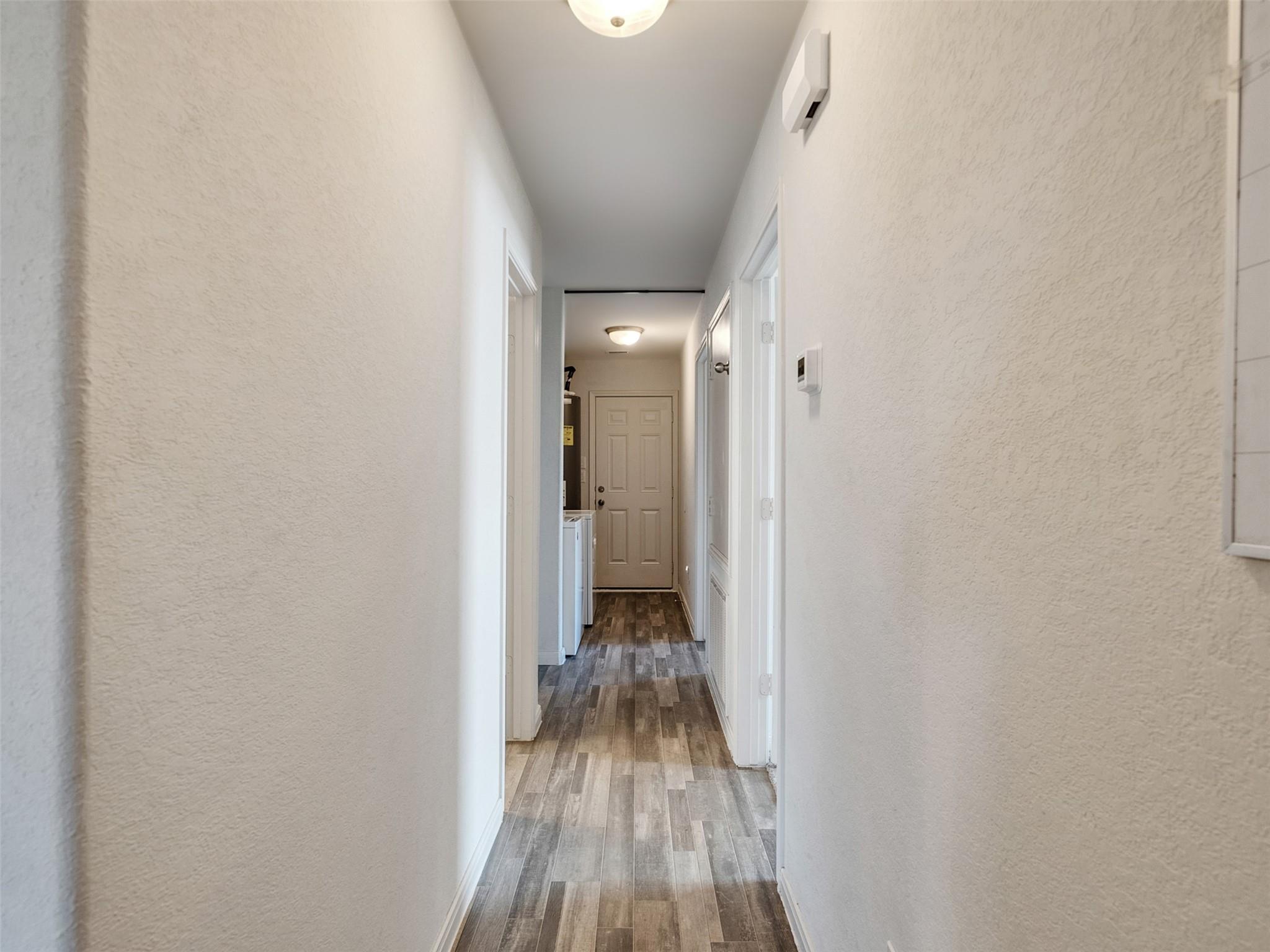 Narrow hallway with wood-look tile flooring and a paneled door at the far end.