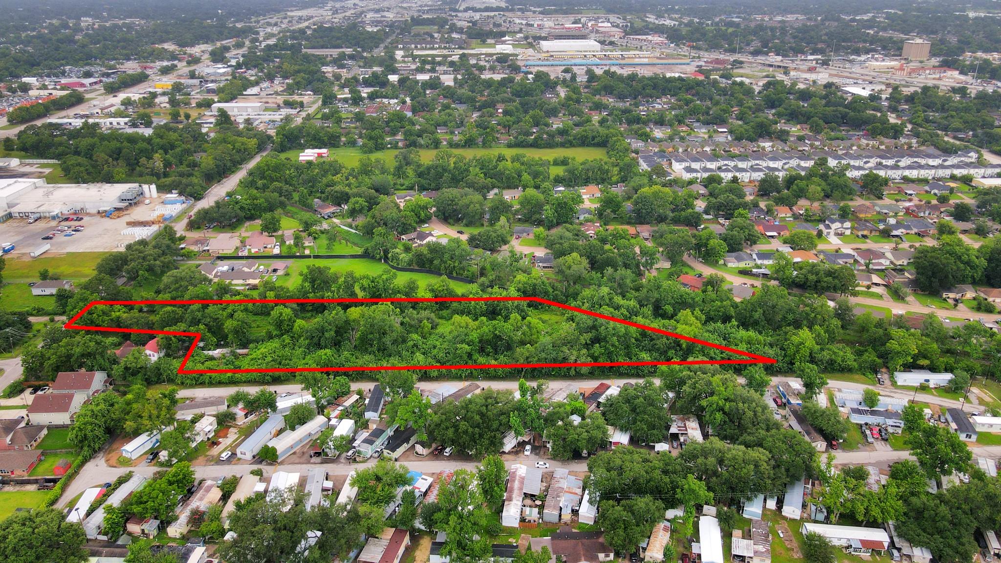 Aerial view of a wooded parcel outlined in red, surrounded by homes and businesses.