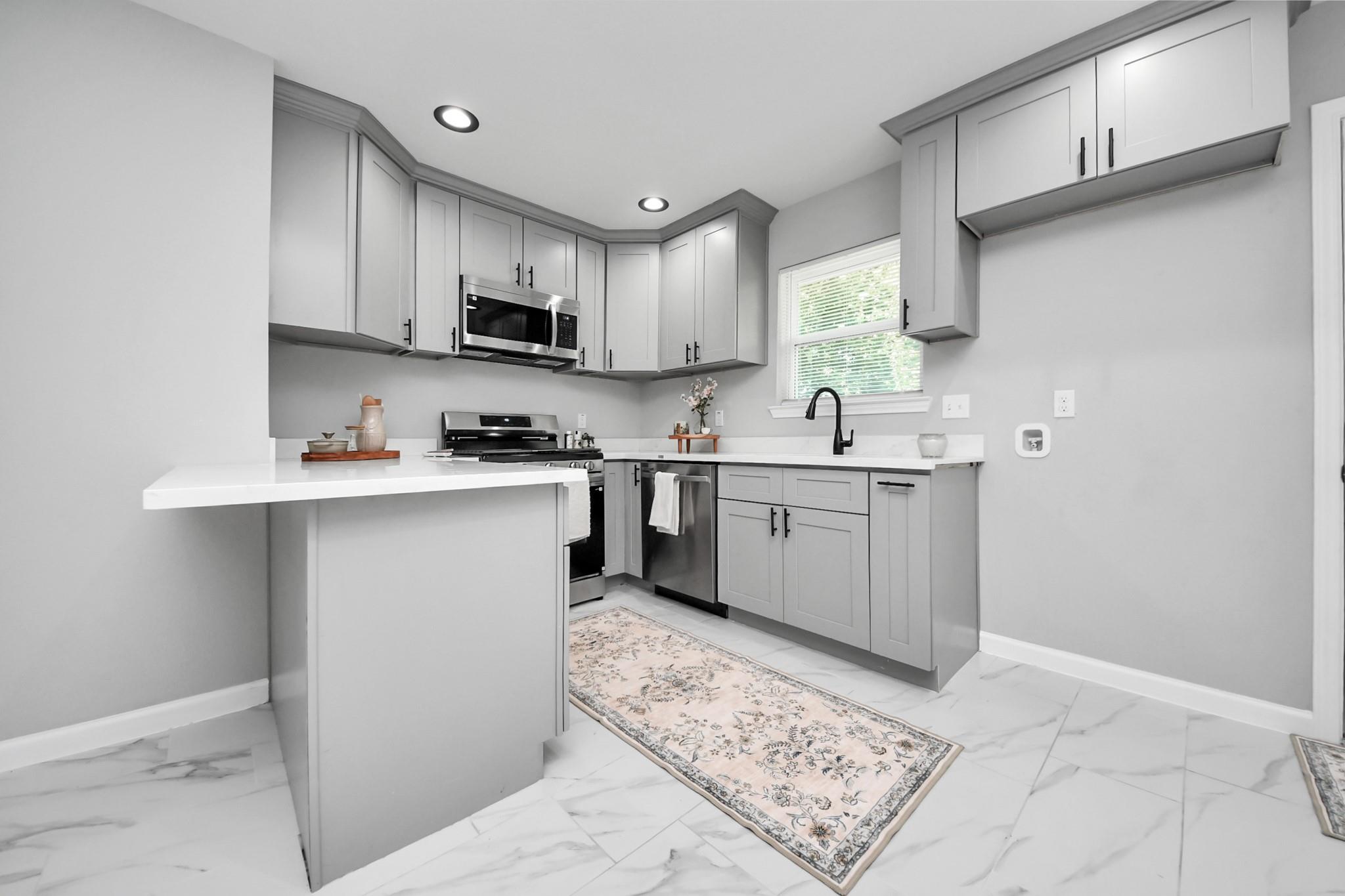 Kitchen with gray shaker cabinets, stainless appliances, and a white peninsula over marble-look tile flooring.
