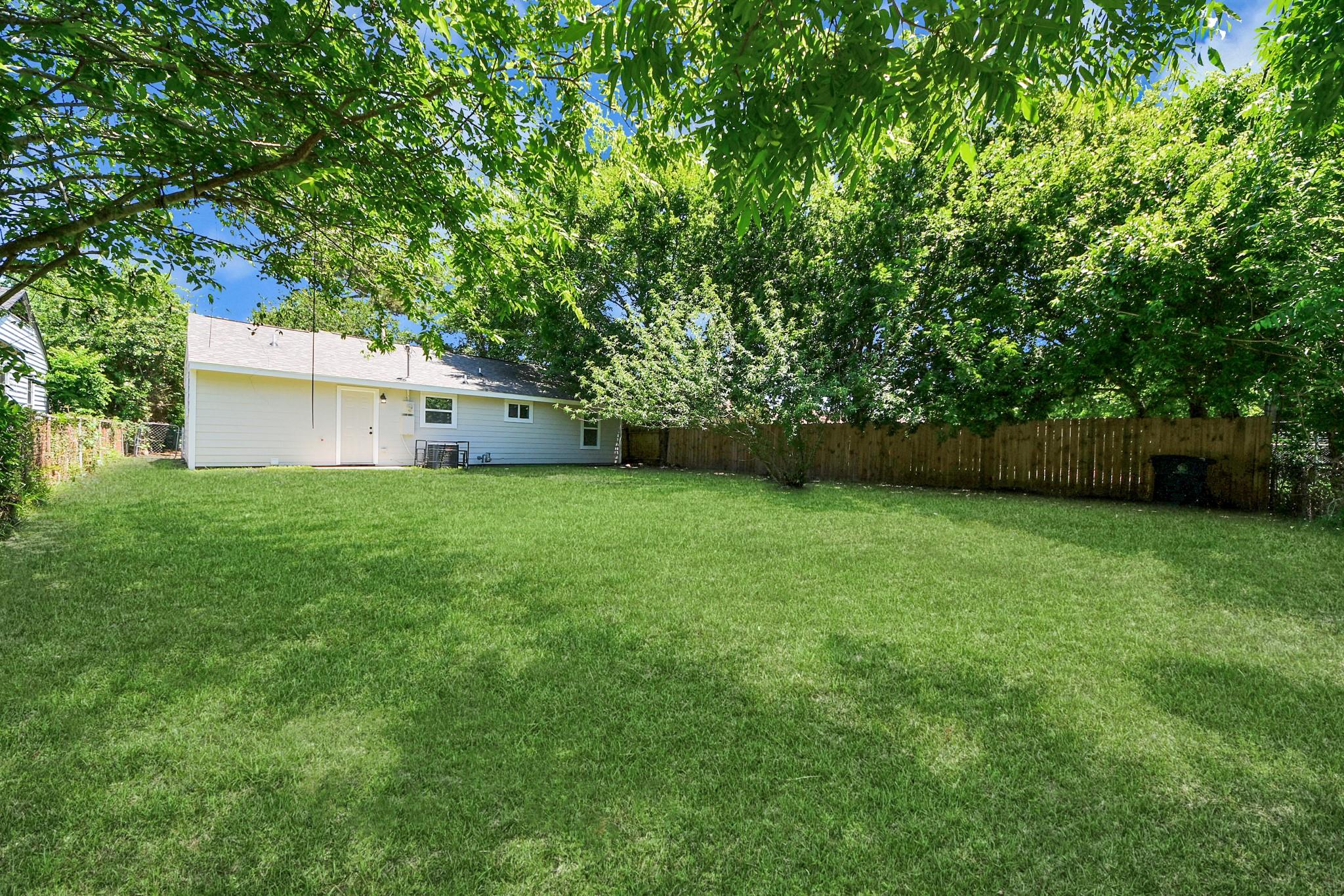House rear and spacious grassy backyard shaded by mature trees and enclosed by a wooden fence.