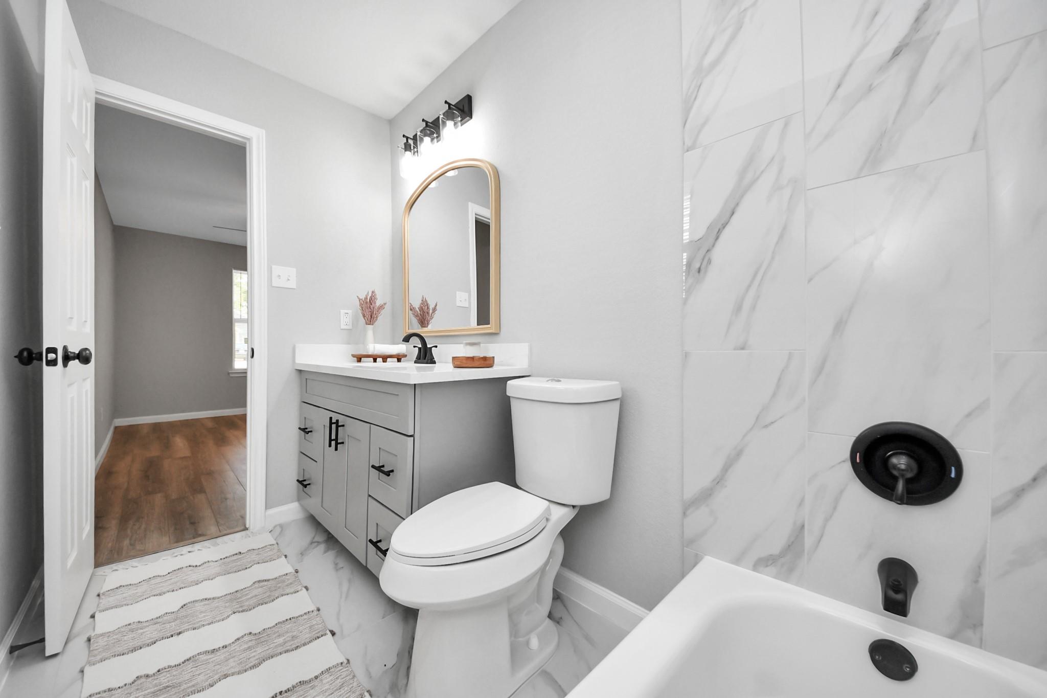 Bathroom with a gray vanity and marble-look tub surround with black fixtures.