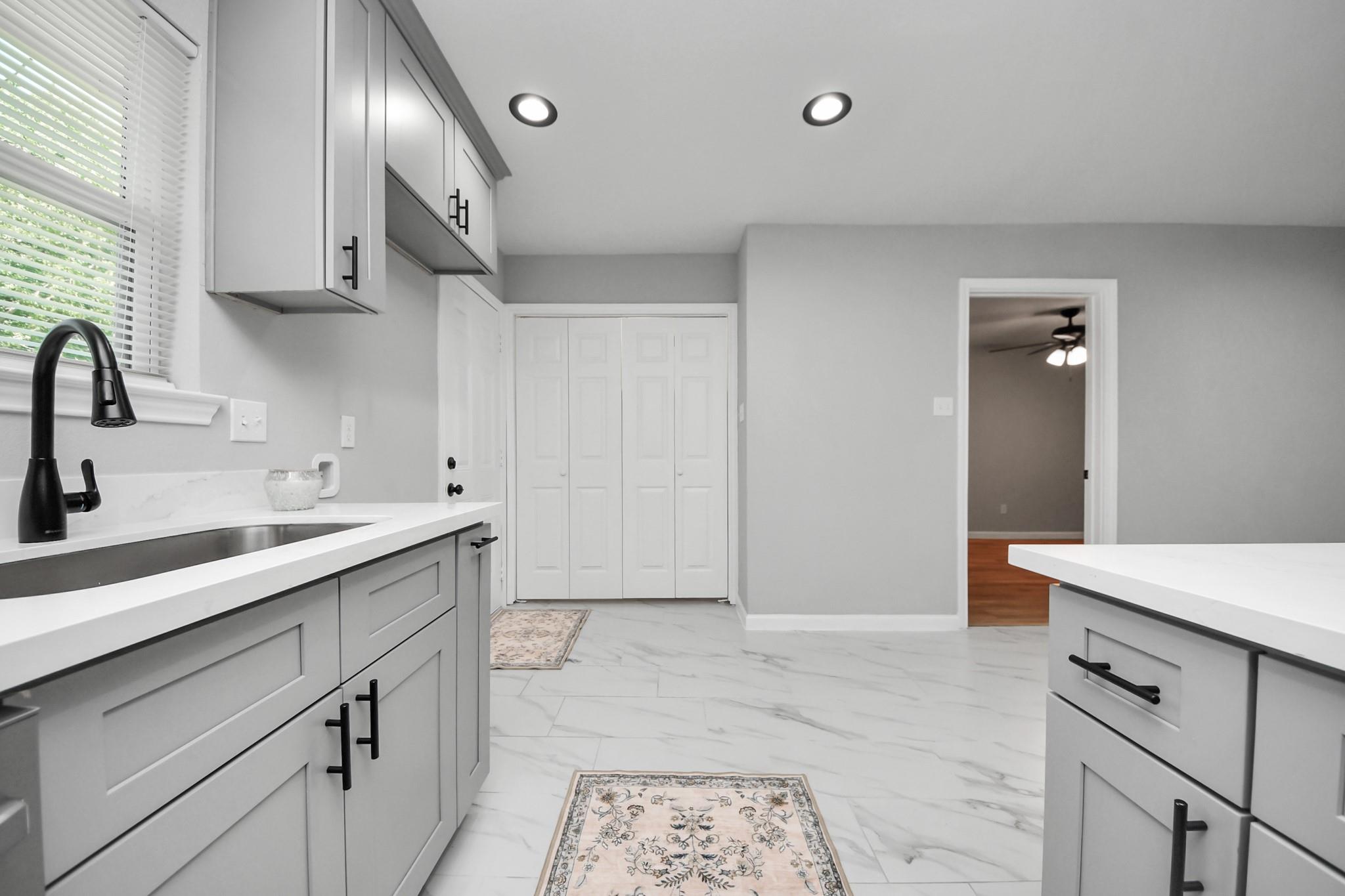 Renovated kitchen with gray cabinets, white counters, black faucet, and marble-look tile floor.