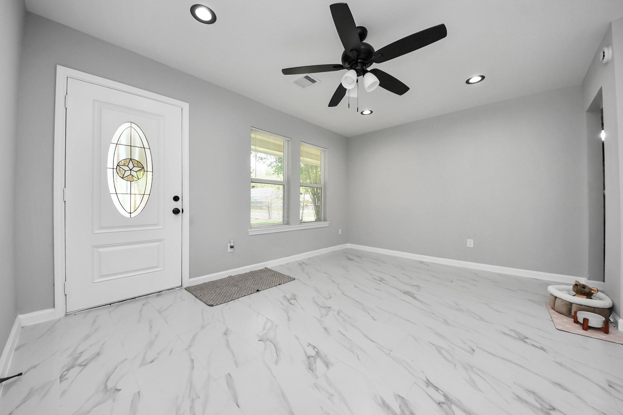 Entry room with decorative-glass front door, marble-look tile, two windows, and a black ceiling fan.