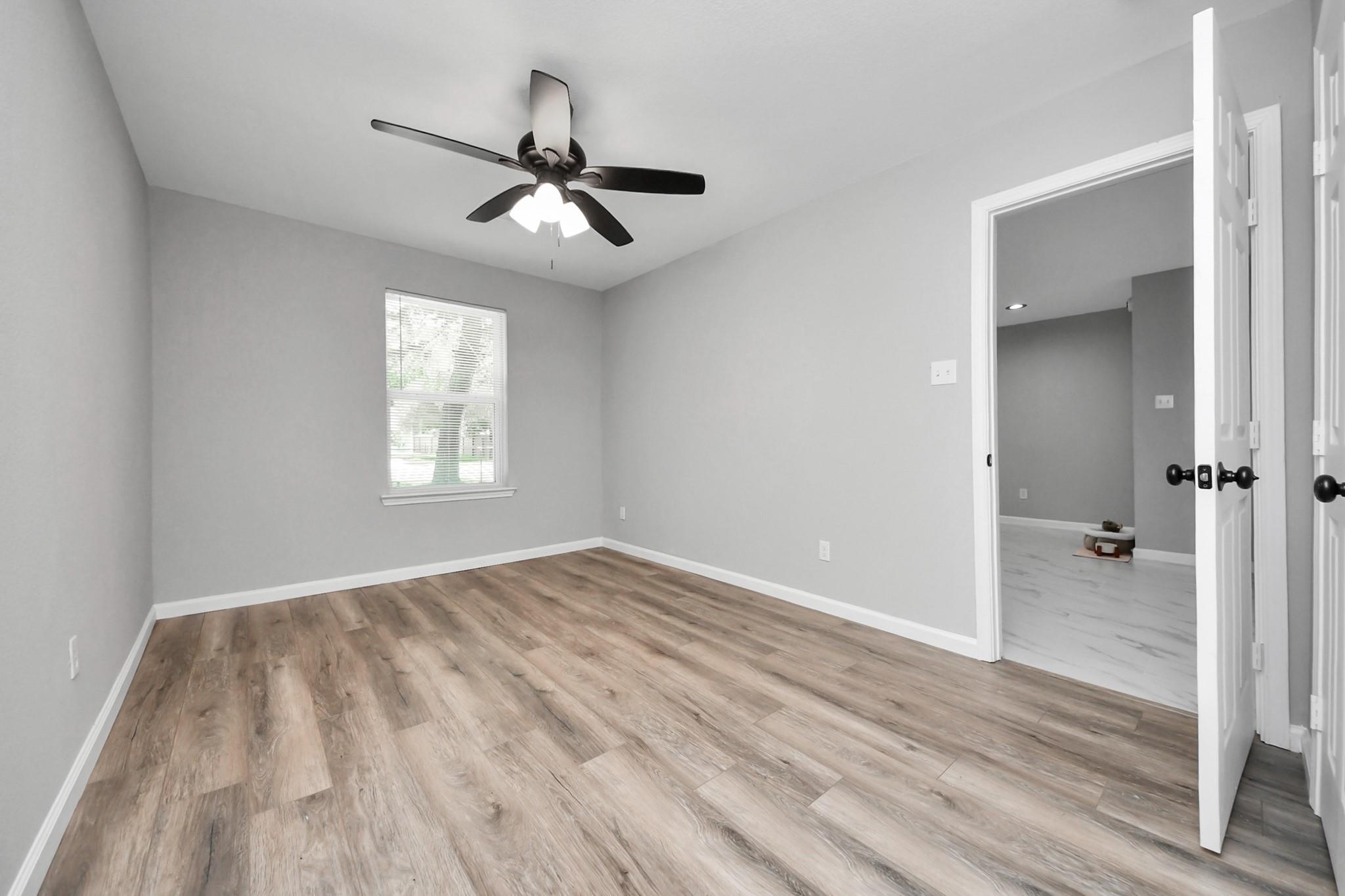 Empty bedroom with wood-look flooring, a ceiling fan, and a window with blinds.