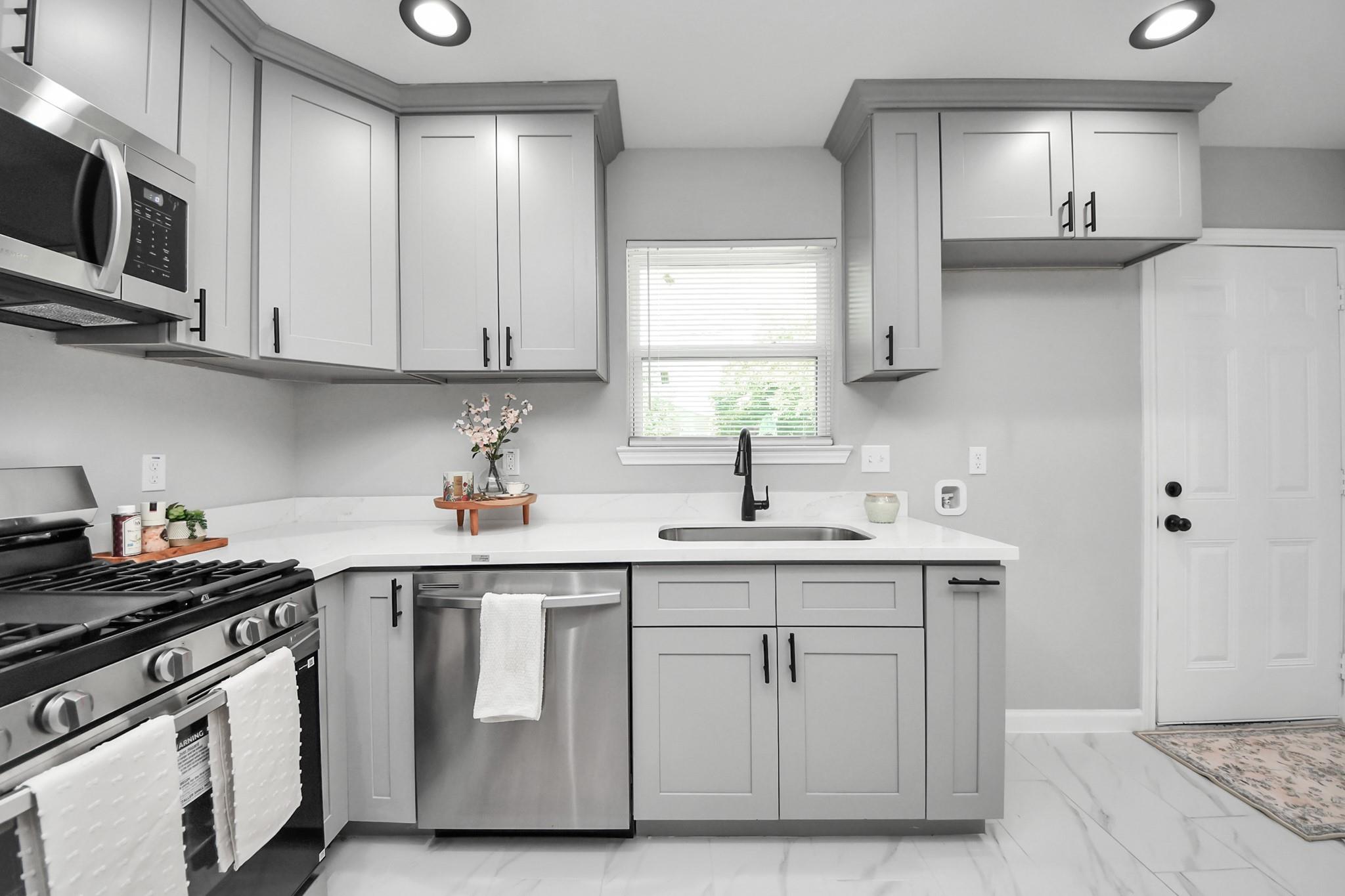 Kitchen with gray shaker cabinets, white counters, stainless appliances and a sink beneath a window.
