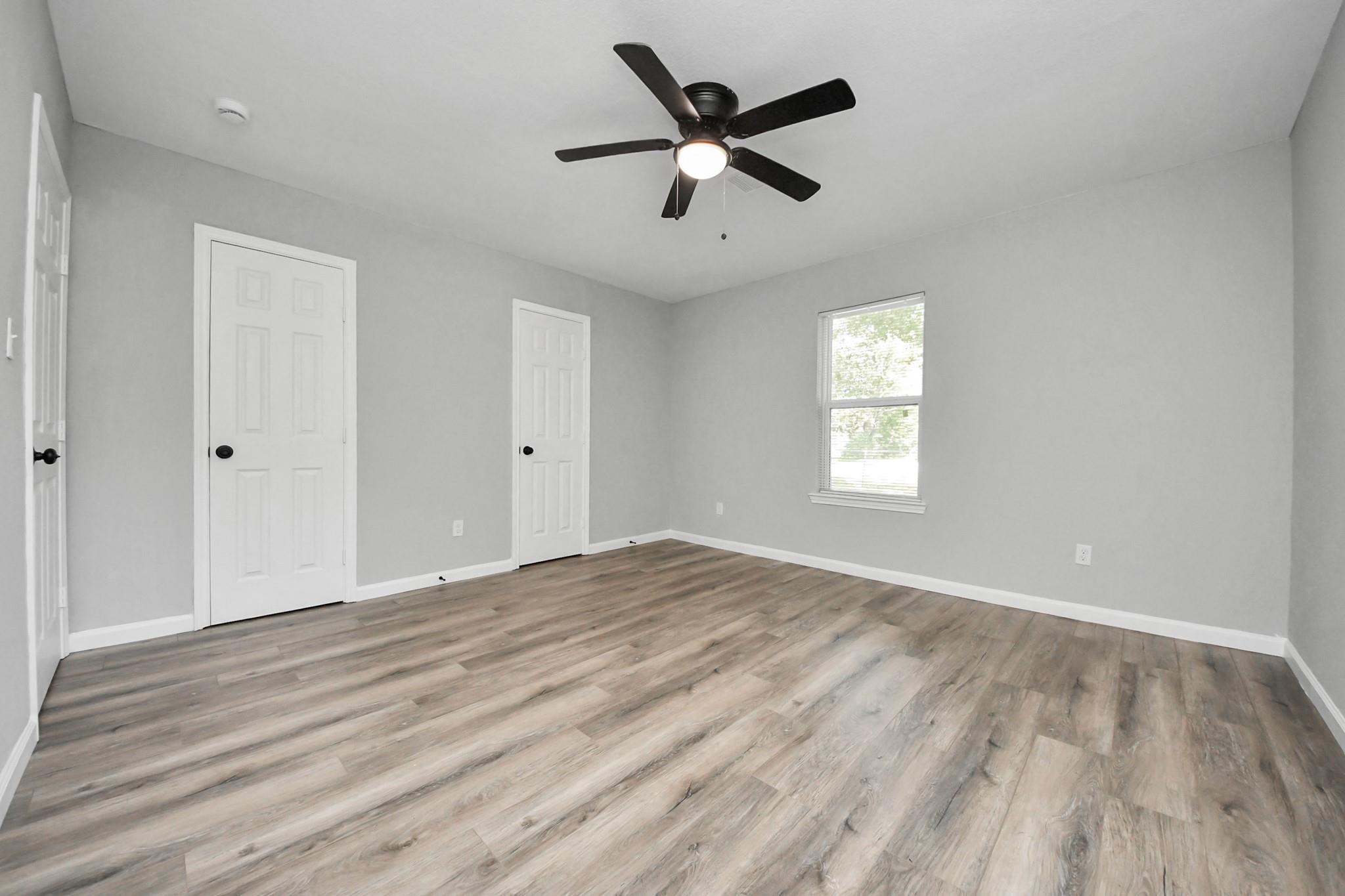 Empty bedroom with gray walls, wood-look flooring, and a black ceiling fan with light.