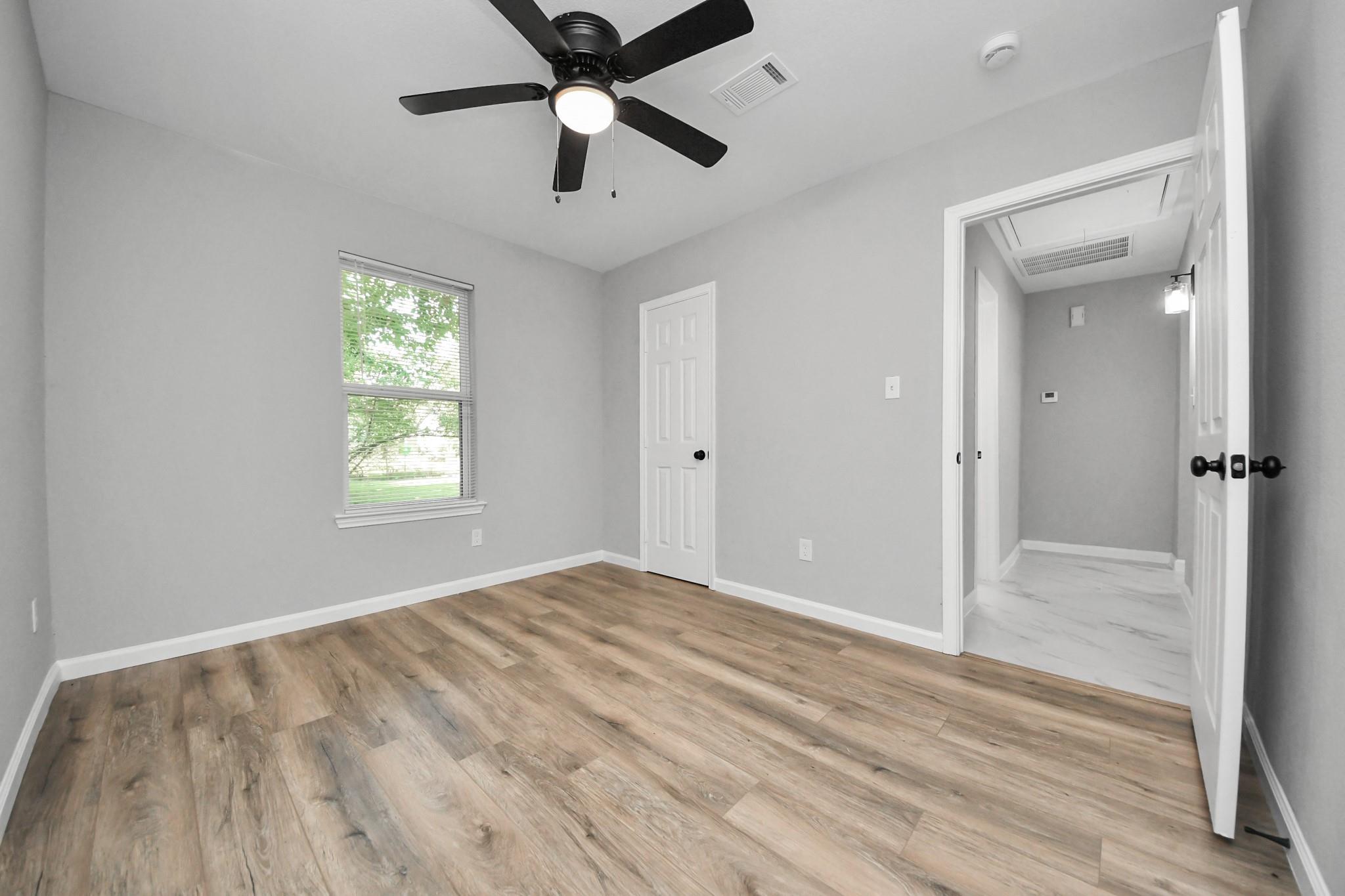 Vacant room with wood-look flooring, a black ceiling fan, and a window with blinds.