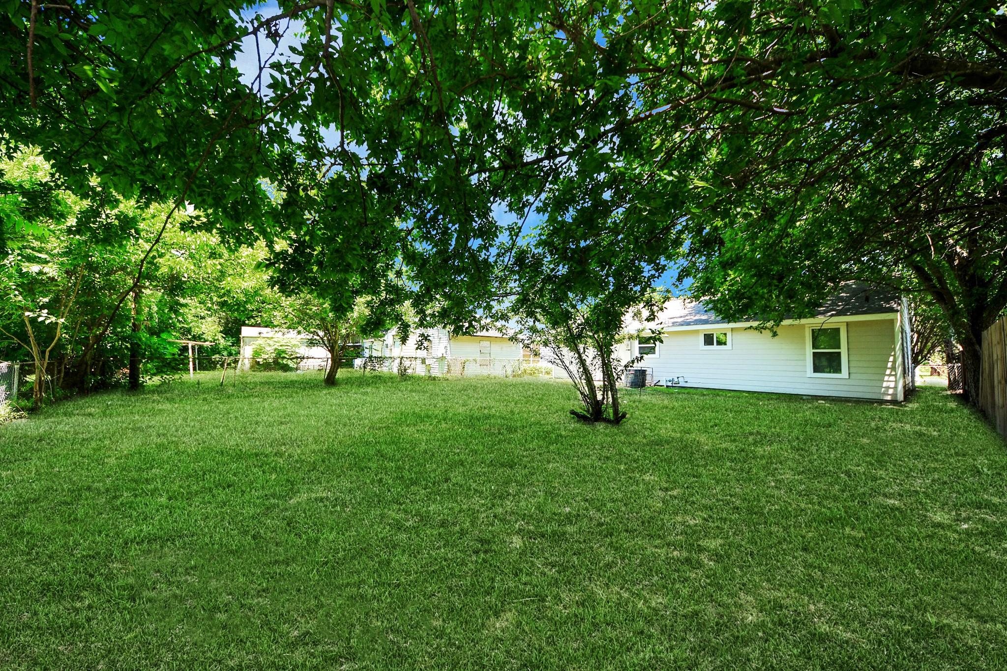 Shady grassy backyard with mature trees and a white-sided house at the far edge.