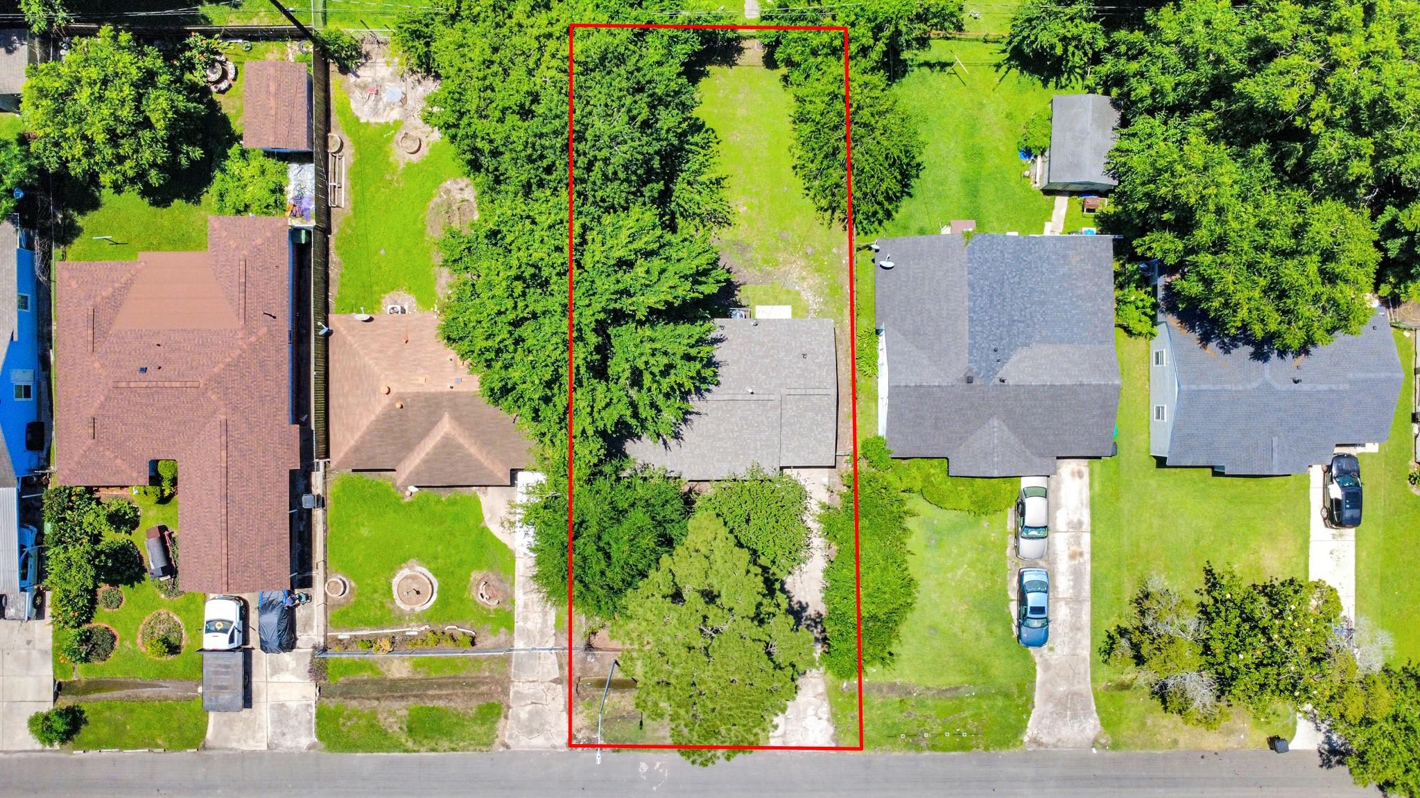 Aerial view of a tree-lined residential lot outlined in red among neighboring homes.