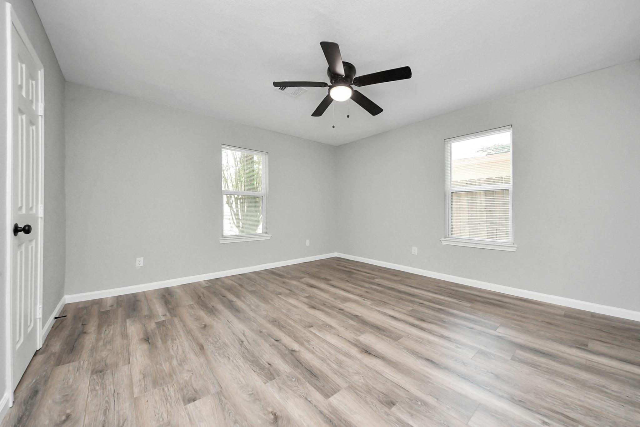 Empty room with plank flooring, two windows, and a black ceiling fan with a light.
