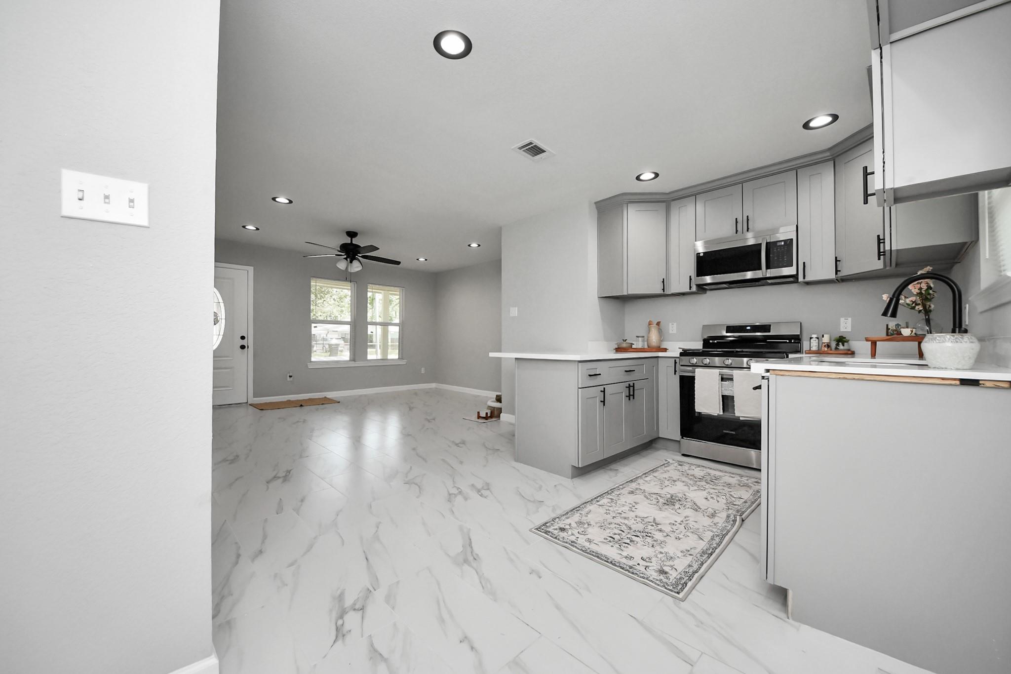 Open-plan kitchen and living area with gray cabinets, stainless steel appliances, and marble-look tile floors.