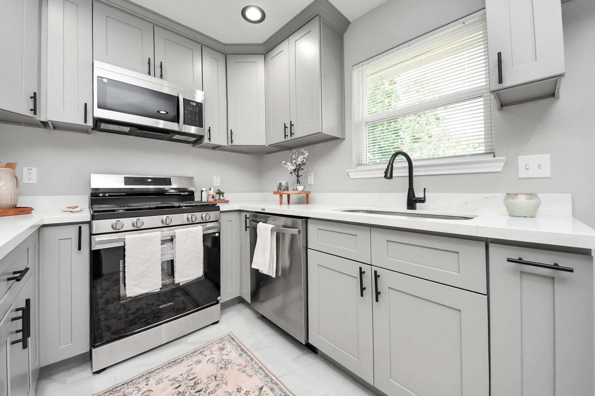Bright kitchen with gray shaker cabinets, stainless appliances, and a black faucet beneath a window.