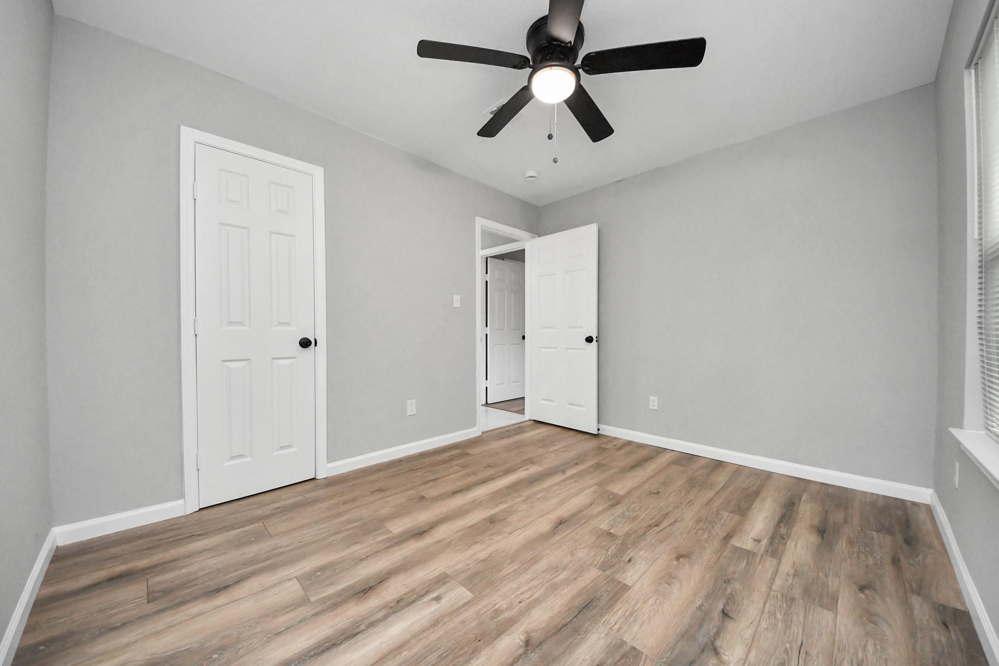 Empty bedroom with wood-look flooring, gray walls, and a black ceiling fan.