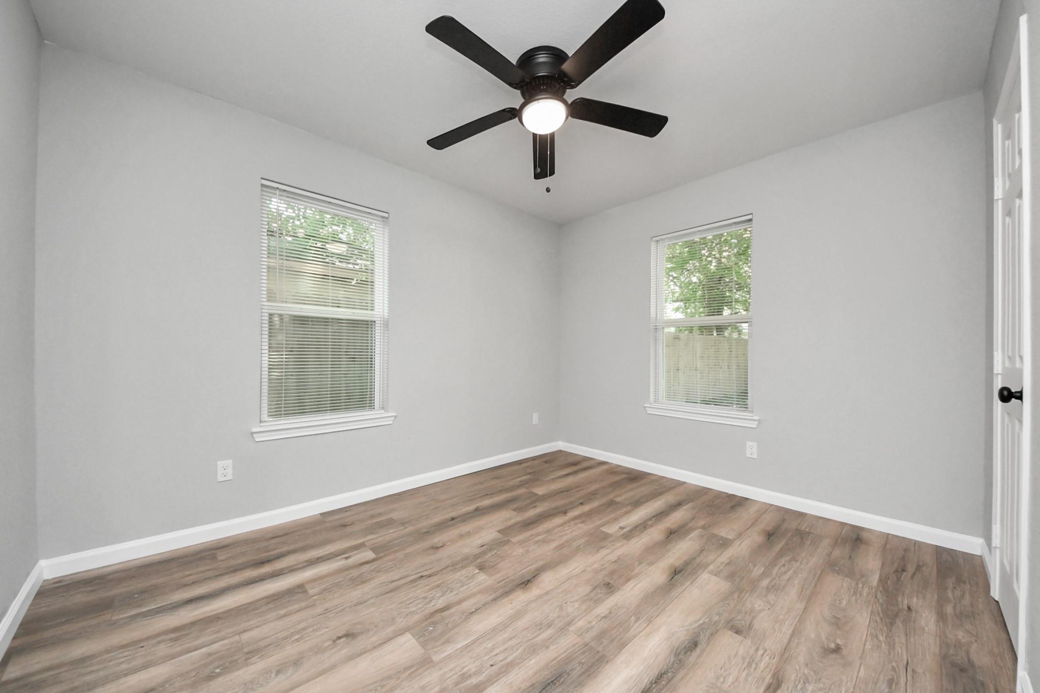 Empty bedroom with wood-look flooring, two blinded windows, and a ceiling fan.