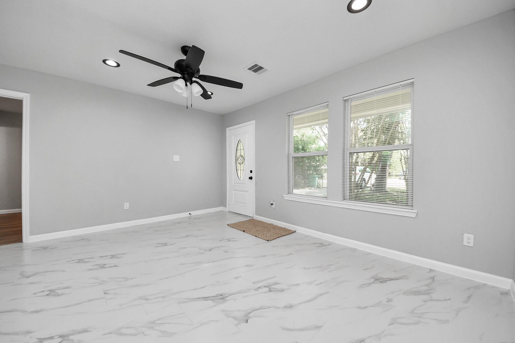 Empty room with marble-look tile floors, a black ceiling fan, two windows, and a white entry door.