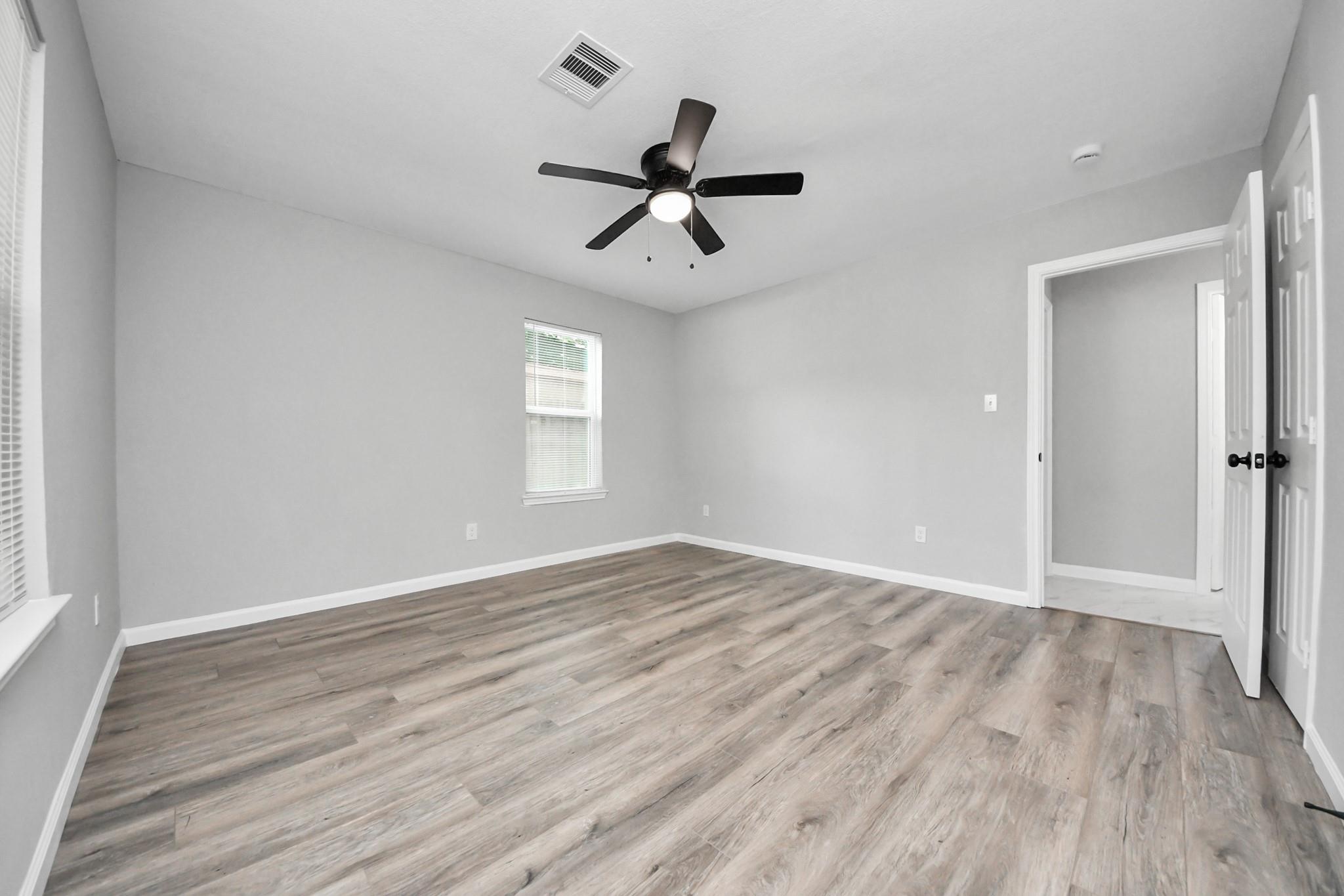 Empty room with plank flooring, a window with blinds, and a black ceiling fan.