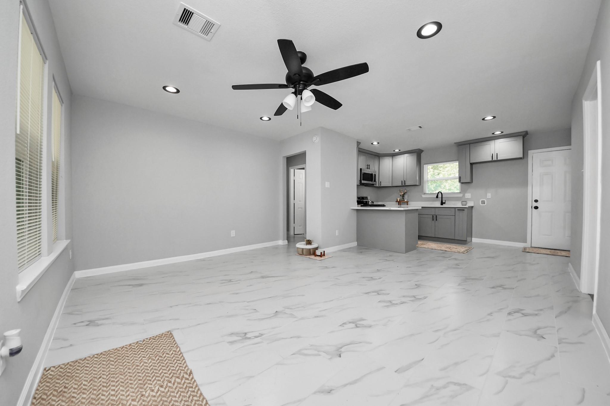 Open-plan living room and kitchen with marble-look tile floors, gray cabinets, and a black ceiling fan.