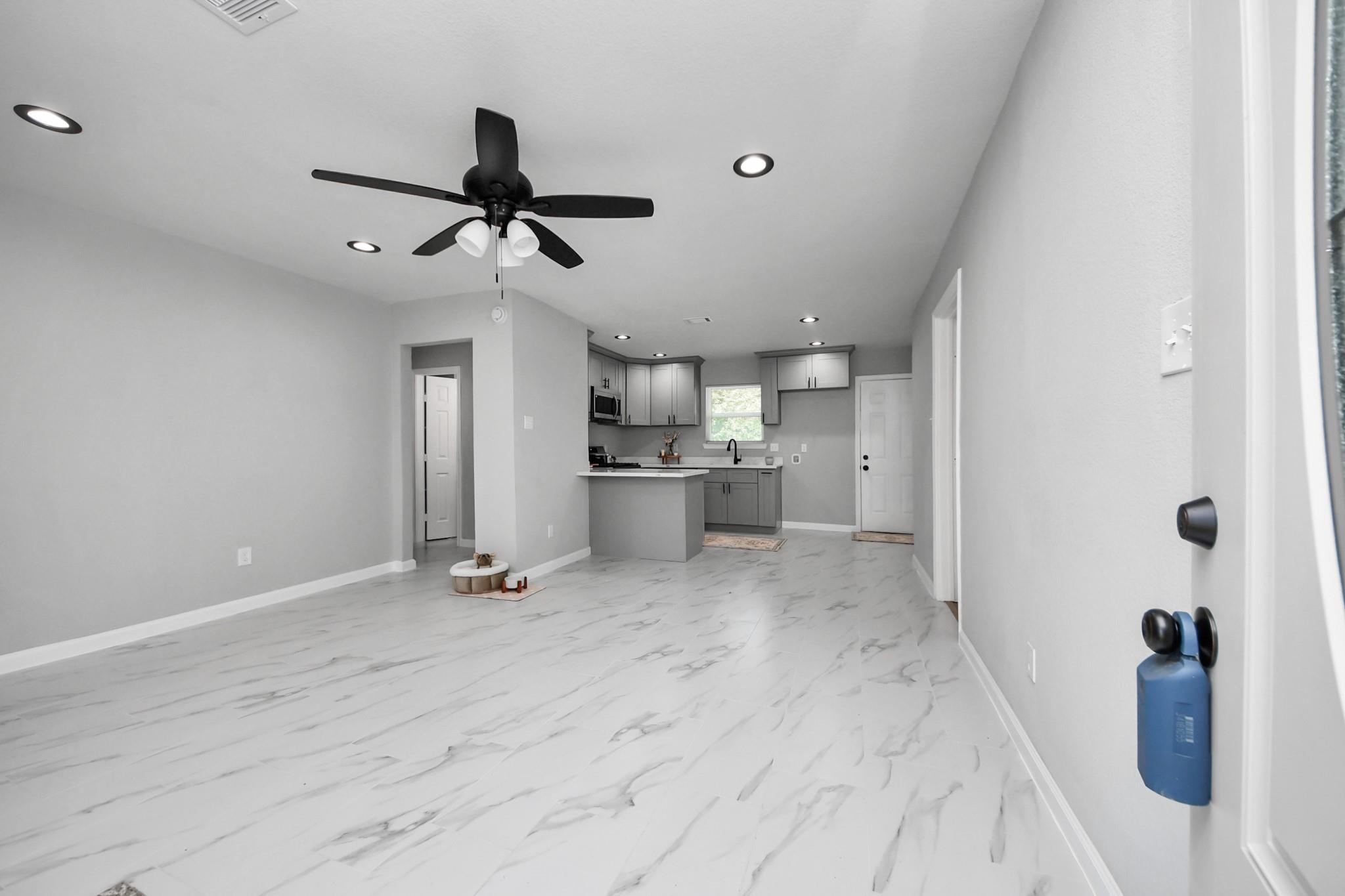 Open living room and kitchen with gray cabinetry, a peninsula, and white marble-look floors.