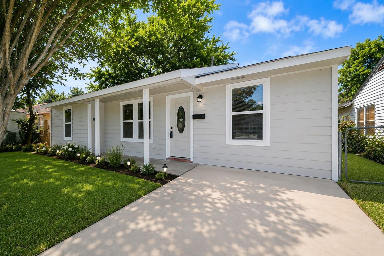 White single-story house with a covered porch, shaded lawn, and wide concrete driveway.