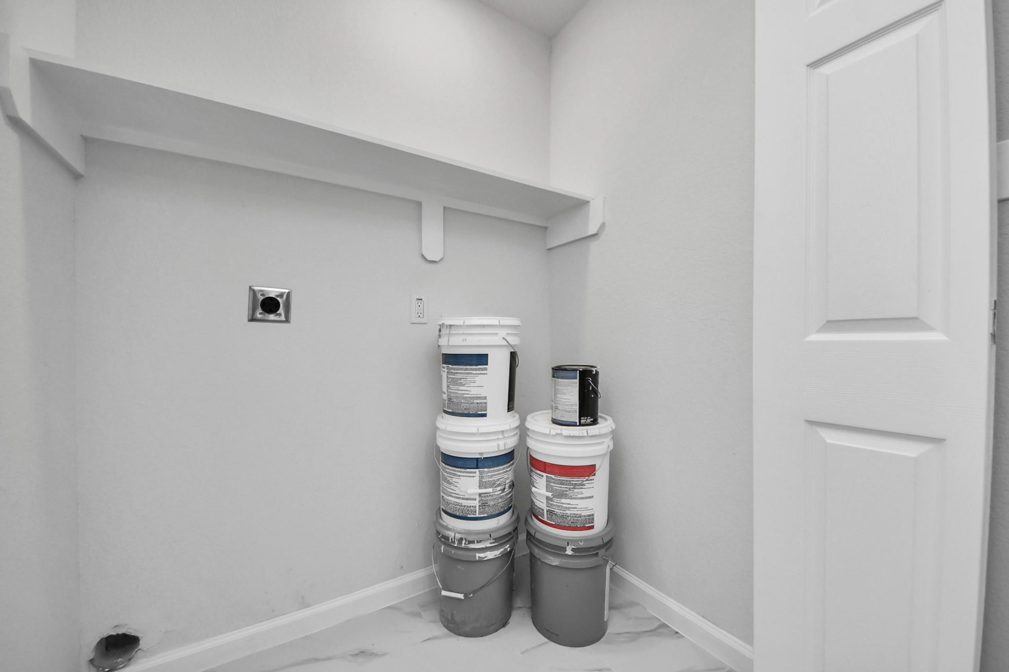 Utility room with a long wall shelf, white door, tiled floor, and stacked paint buckets.