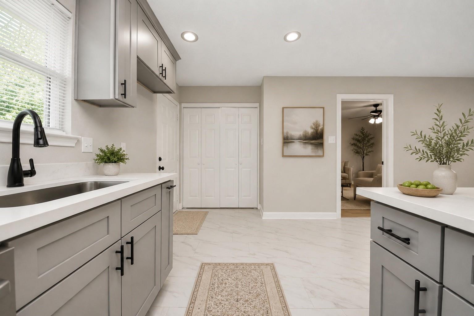 Kitchen with gray cabinets, white countertops, black faucet, and an opening to a sitting room.