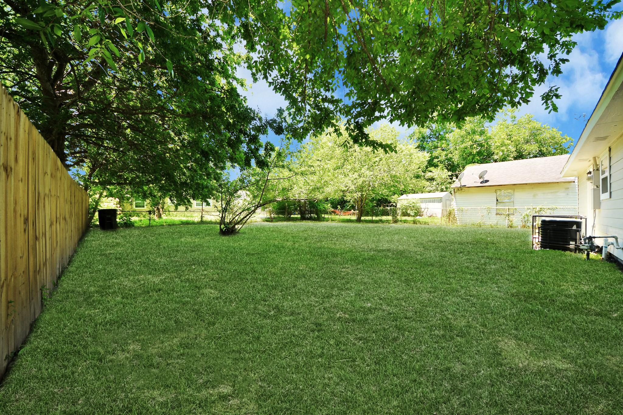 Grassy backyard with mature shade trees, a wooden fence, and the house along one side.