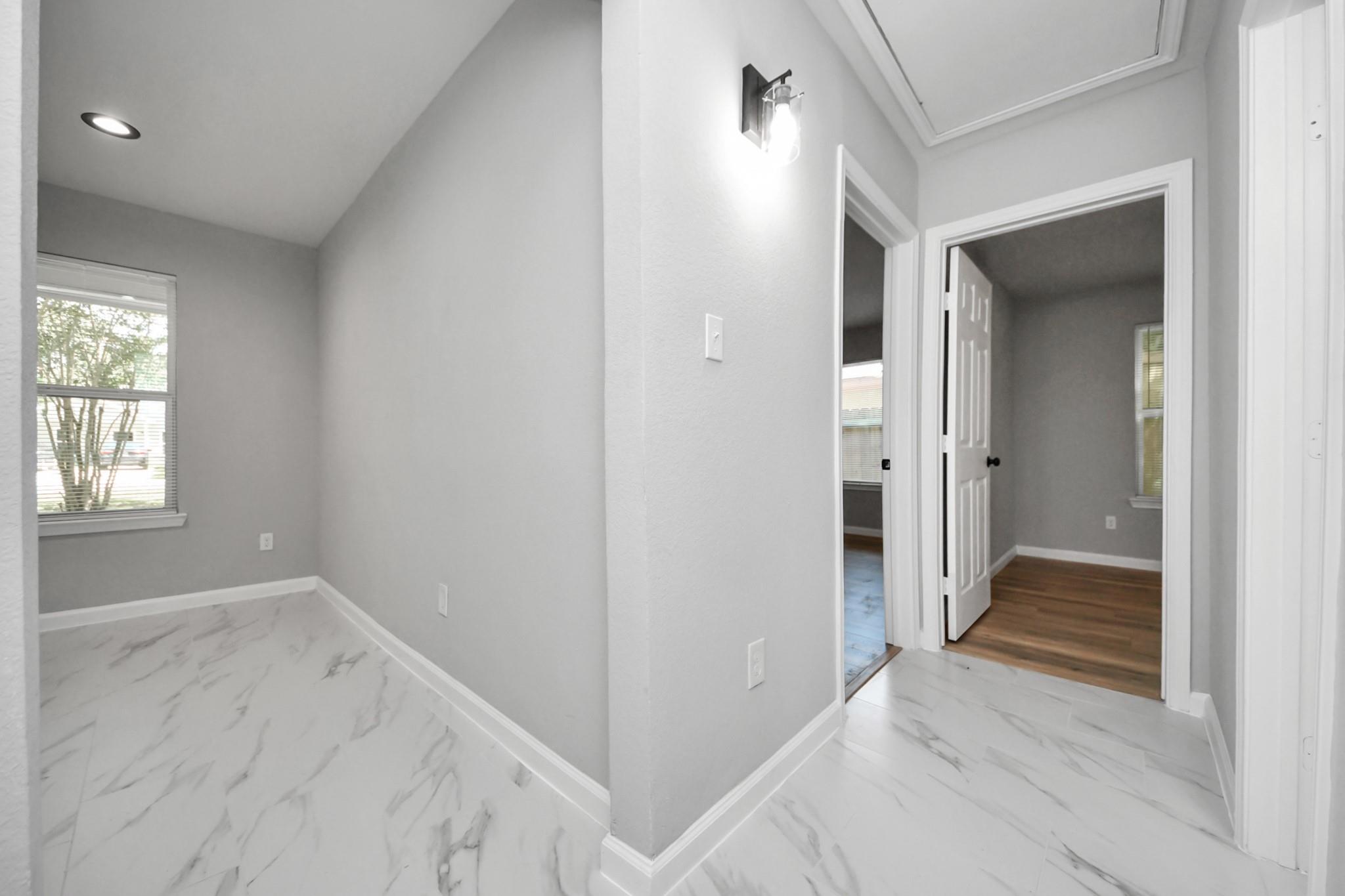 Hallway with marble-look tile, gray walls, and doorways to rooms with wood flooring.