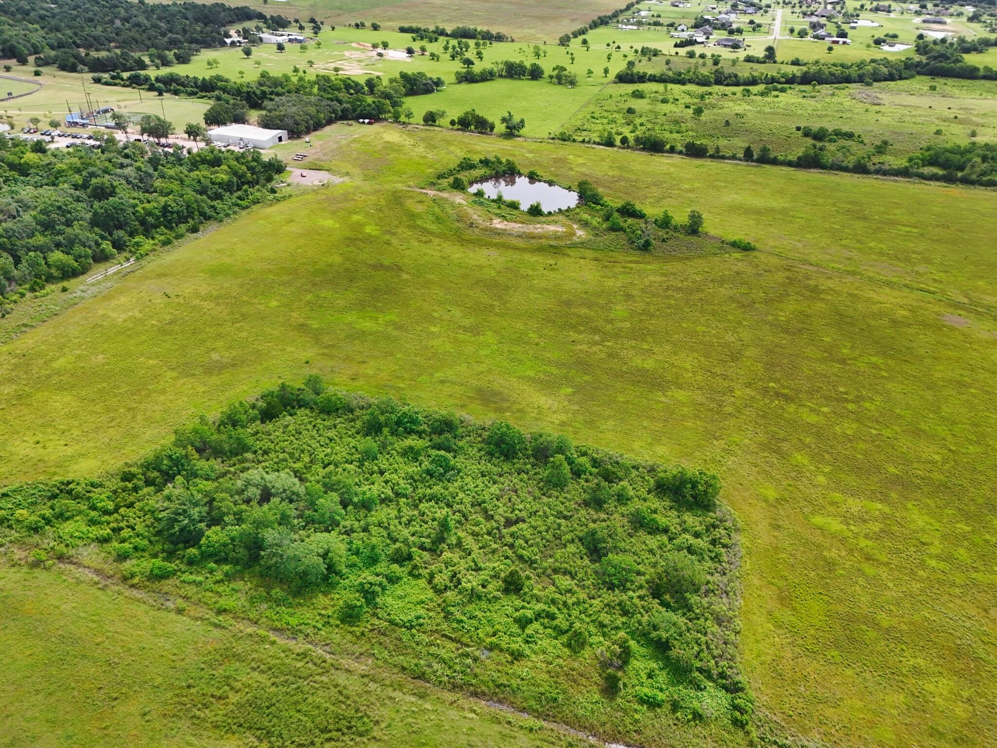 Aerial view of grassy acreage with a pond and a large wooded area.