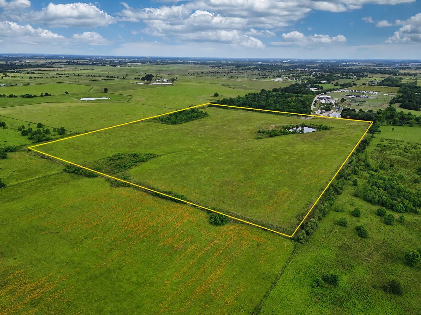 Aerial view of a yellow-outlined rural land parcel with open pasture and a small pond.