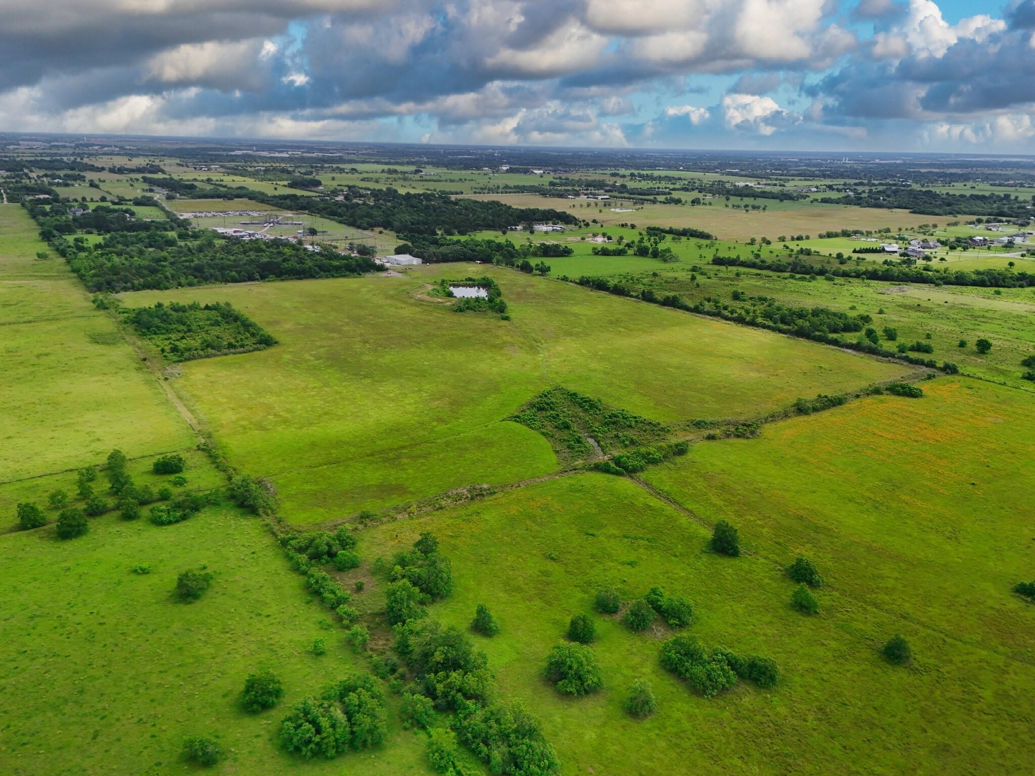 Aerial view of green pasture with tree-lined drainage areas and a small pond.