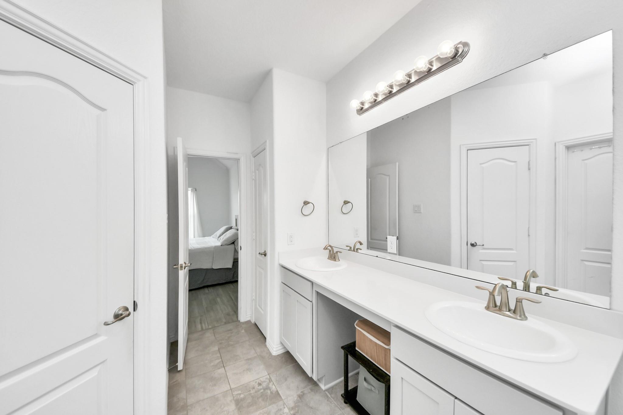 Bathroom with a long double-sink vanity, large mirror, and gray tile floor.