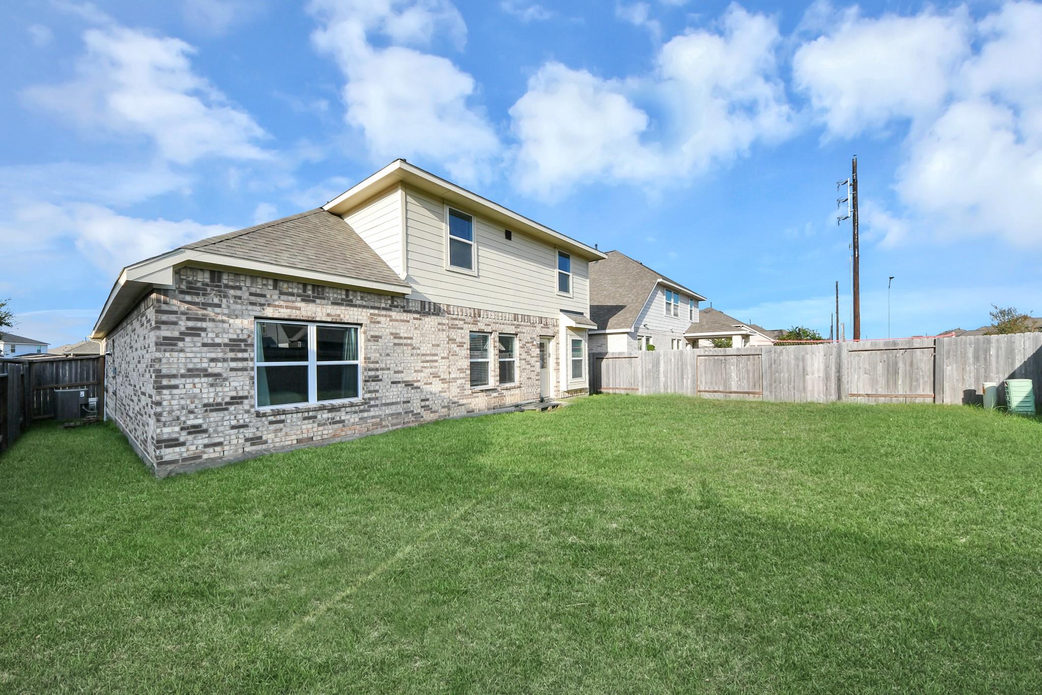 Two-story home with brick and siding overlooking a spacious fenced backyard with green lawn.