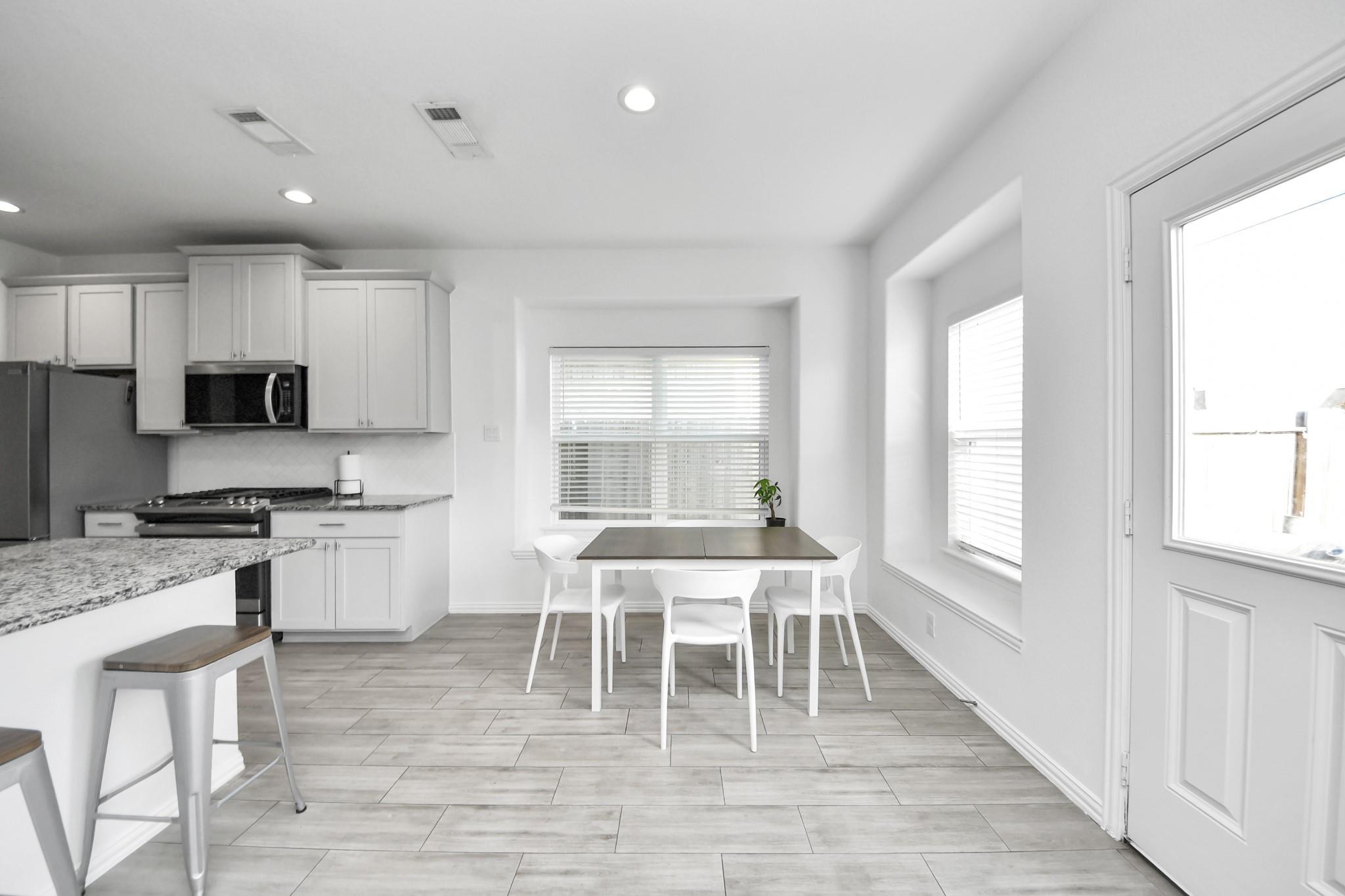 Kitchen and dining area with white cabinetry, granite counters, and a table beside large windows.