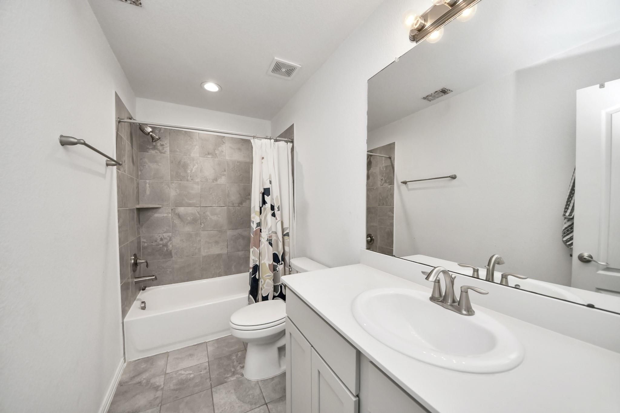 Bathroom with a white vanity, large mirror, and gray-tiled tub and shower.