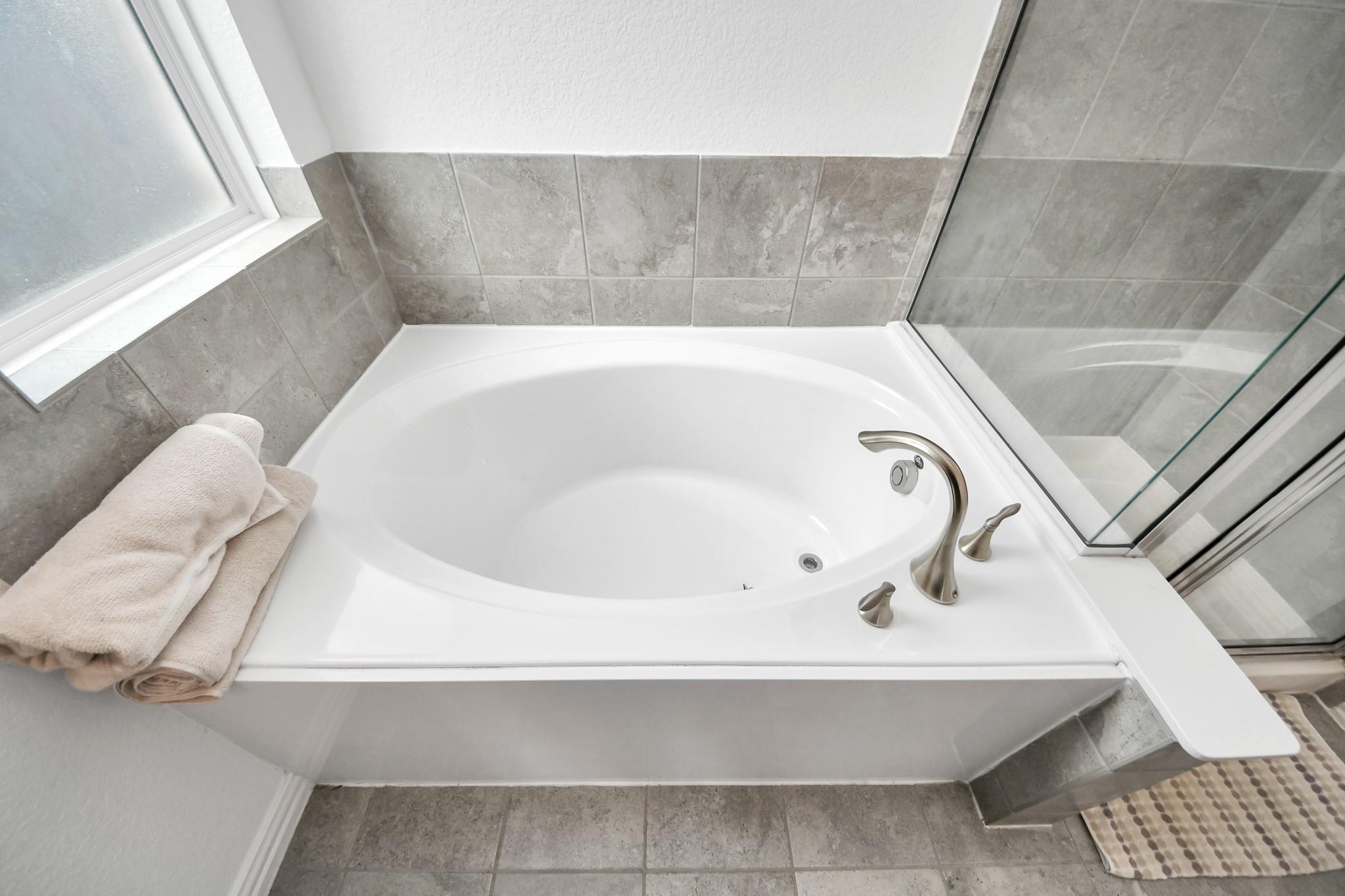 White soaking tub with brushed metal fixtures, gray tile surround, and glass shower enclosure.