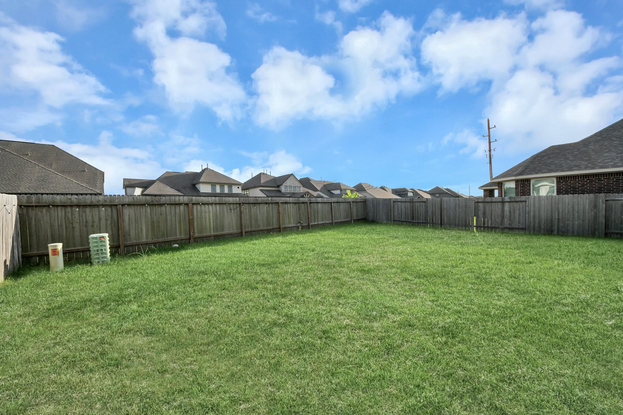 Grassy backyard enclosed by a wooden privacy fence, with neighboring homes visible beyond it.